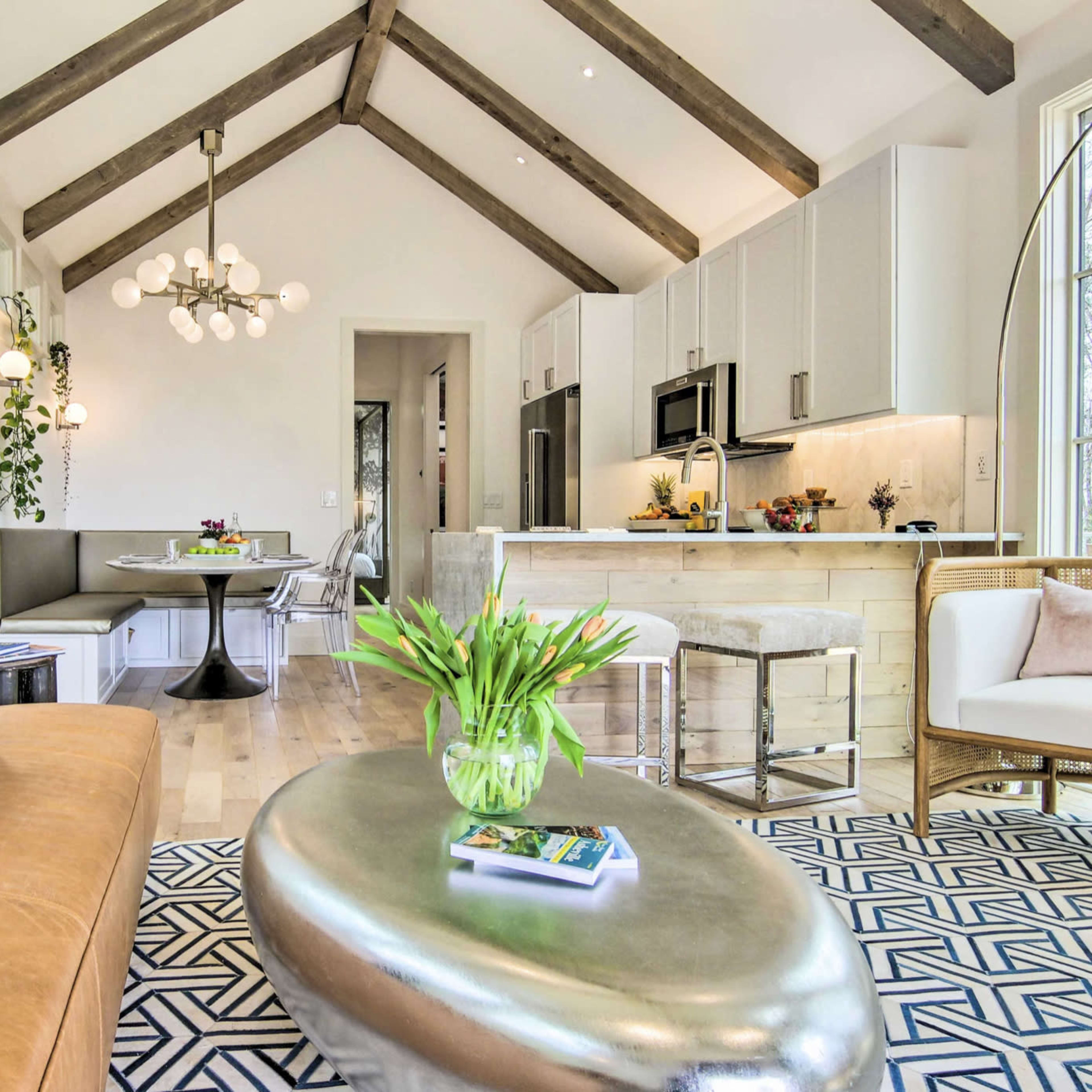 A modern living space featuring a brown leather sofa, a circular metallic coffee table, and a kitchenette with light cabinetry and a dining area.
