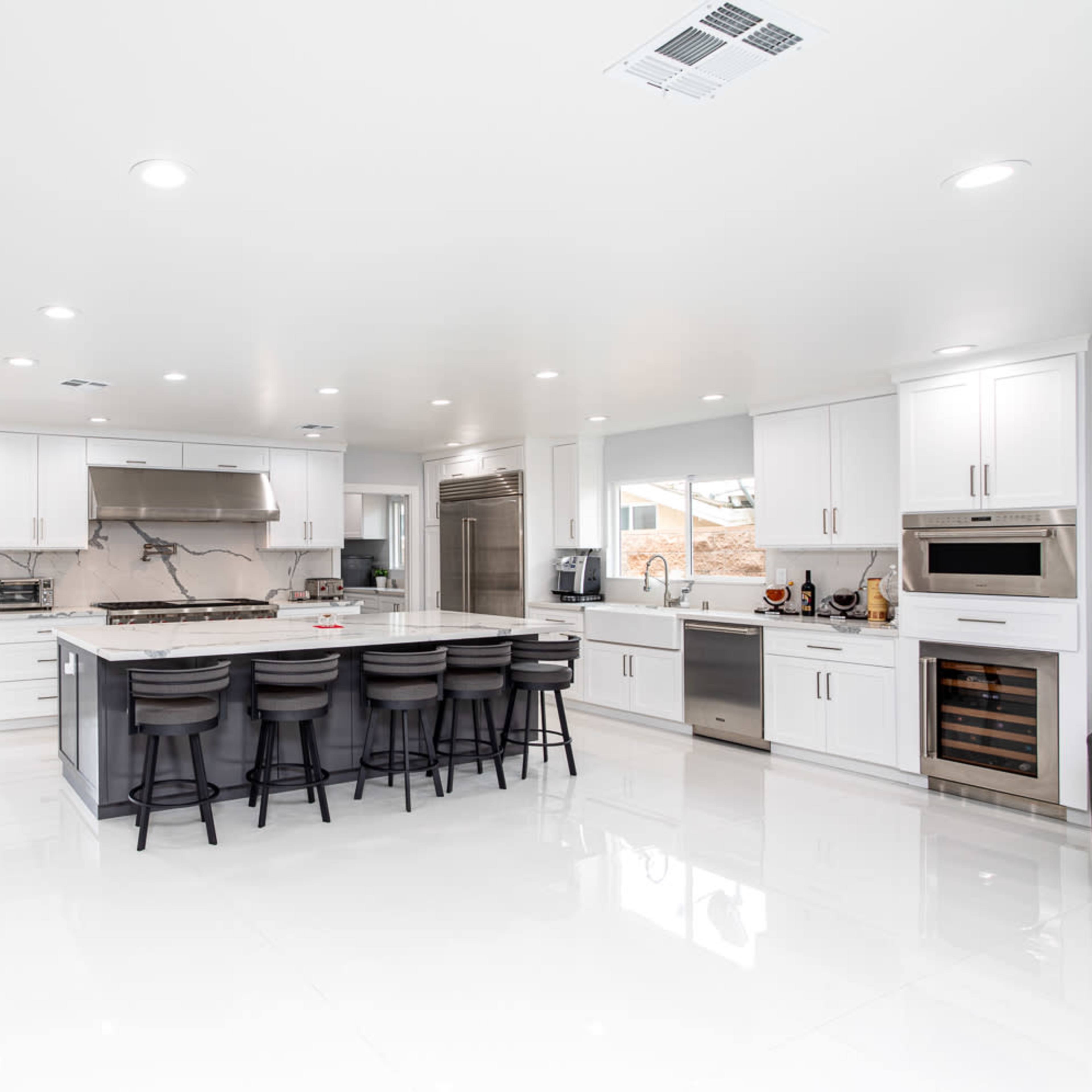 A modern kitchen features an island with bar seating, stainless steel appliances, and white cabinetry, illuminated by recessed lighting.