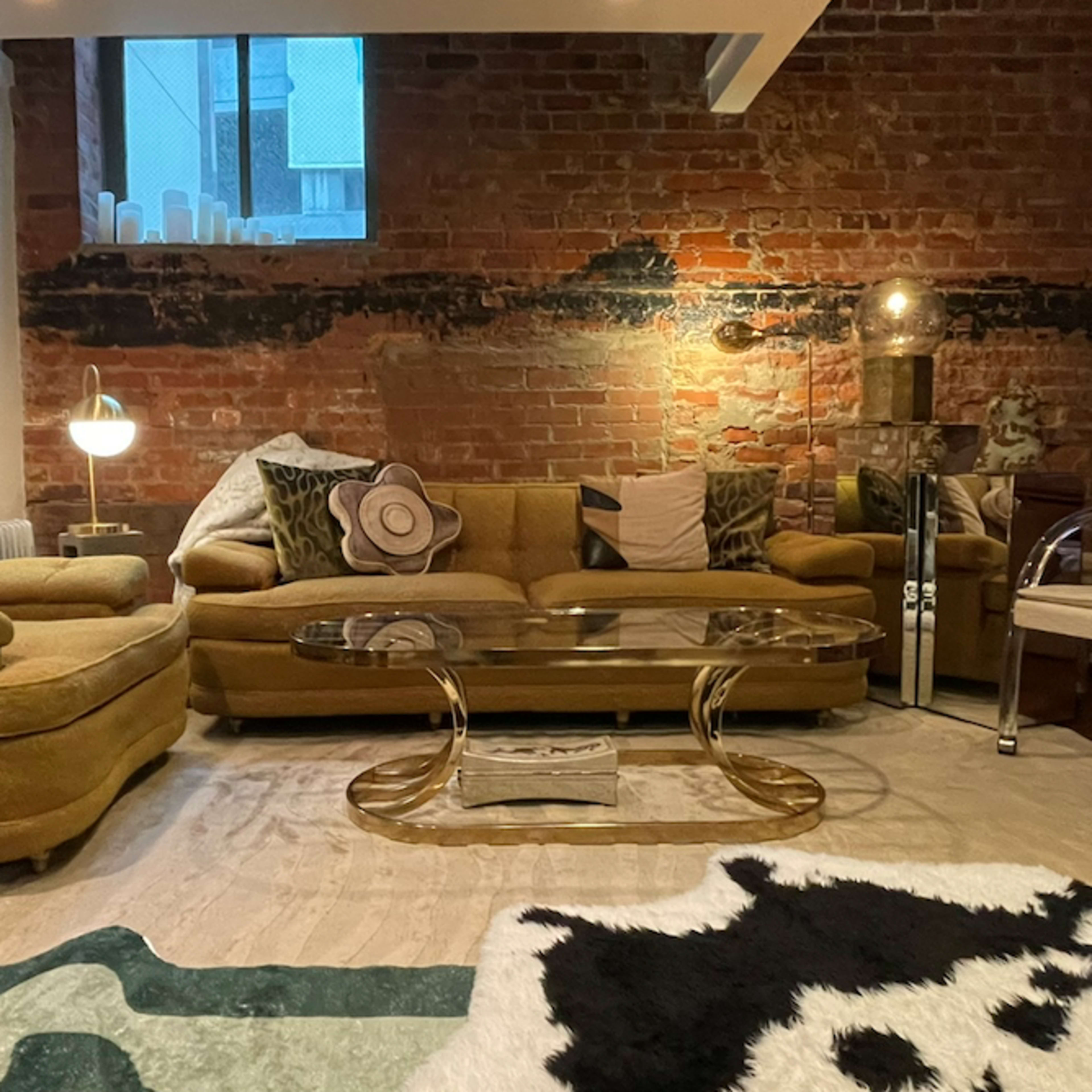 The living area features a pair of yellow sofas, a glass coffee table, and a cowhide rug, complemented by exposed brick walls and various decorative pillows.