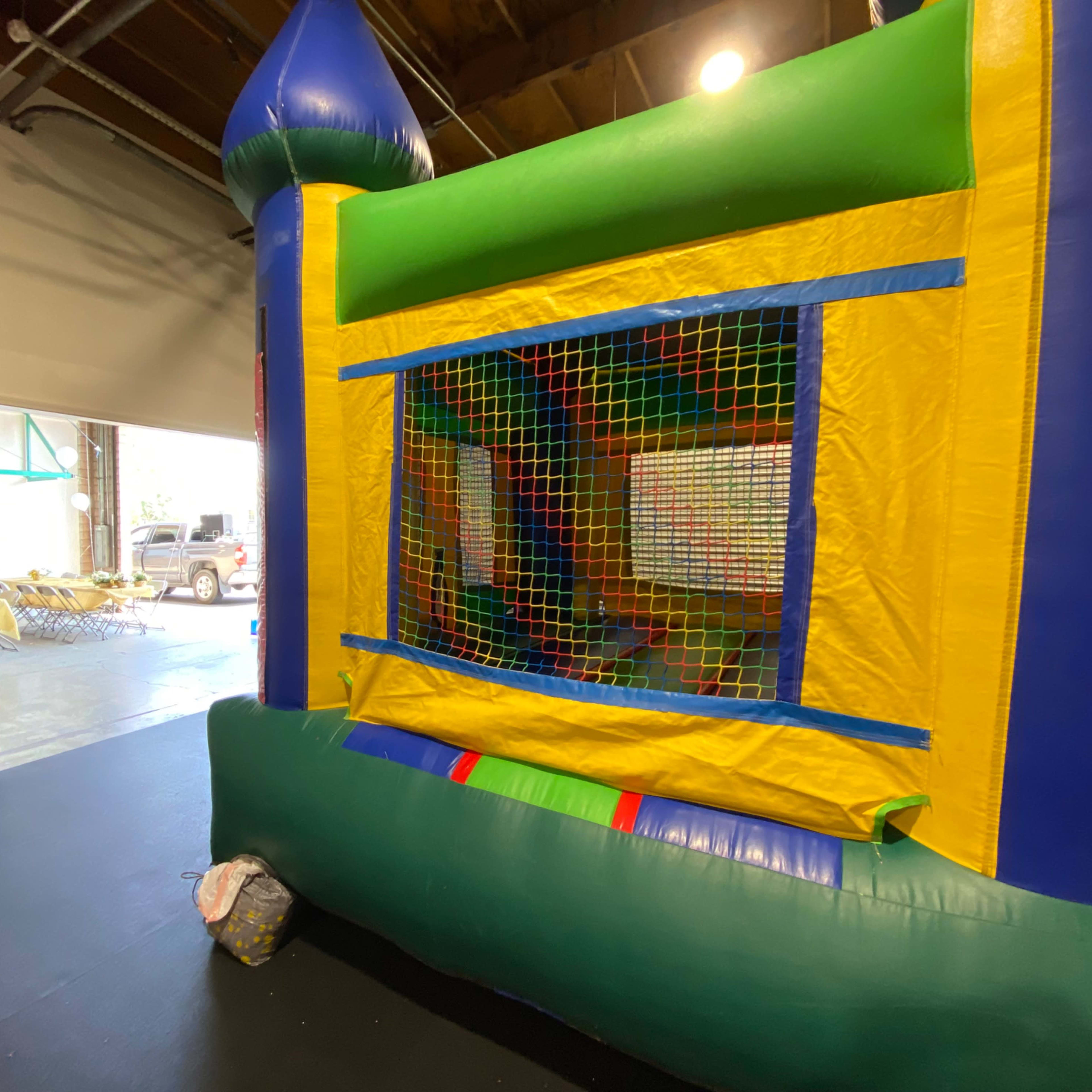 A colorful bounce house with a netted opening is positioned in an indoor space next to an open door.