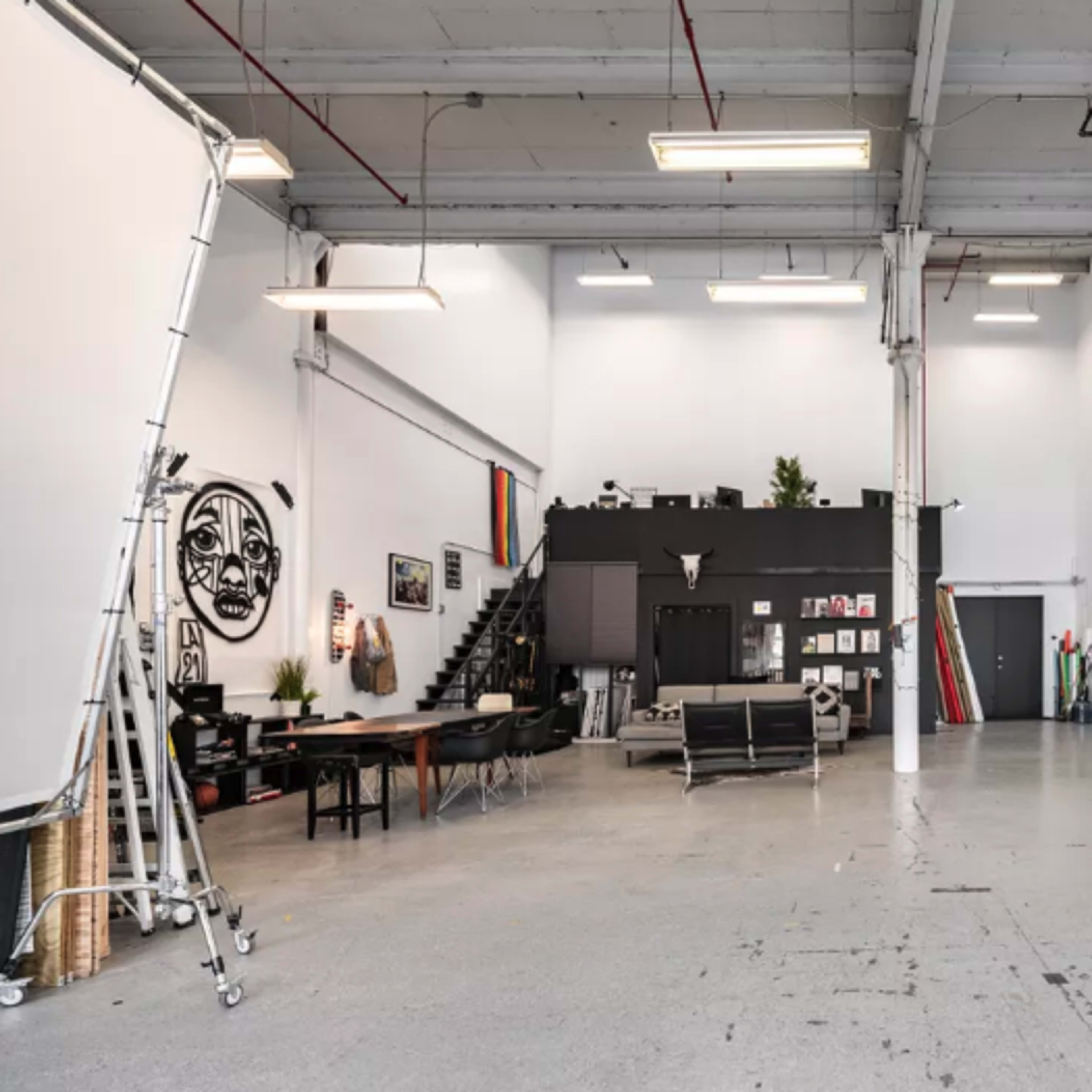 A spacious, well-lit studio with white walls, a black feature wall, a large table, and various artworks displayed.