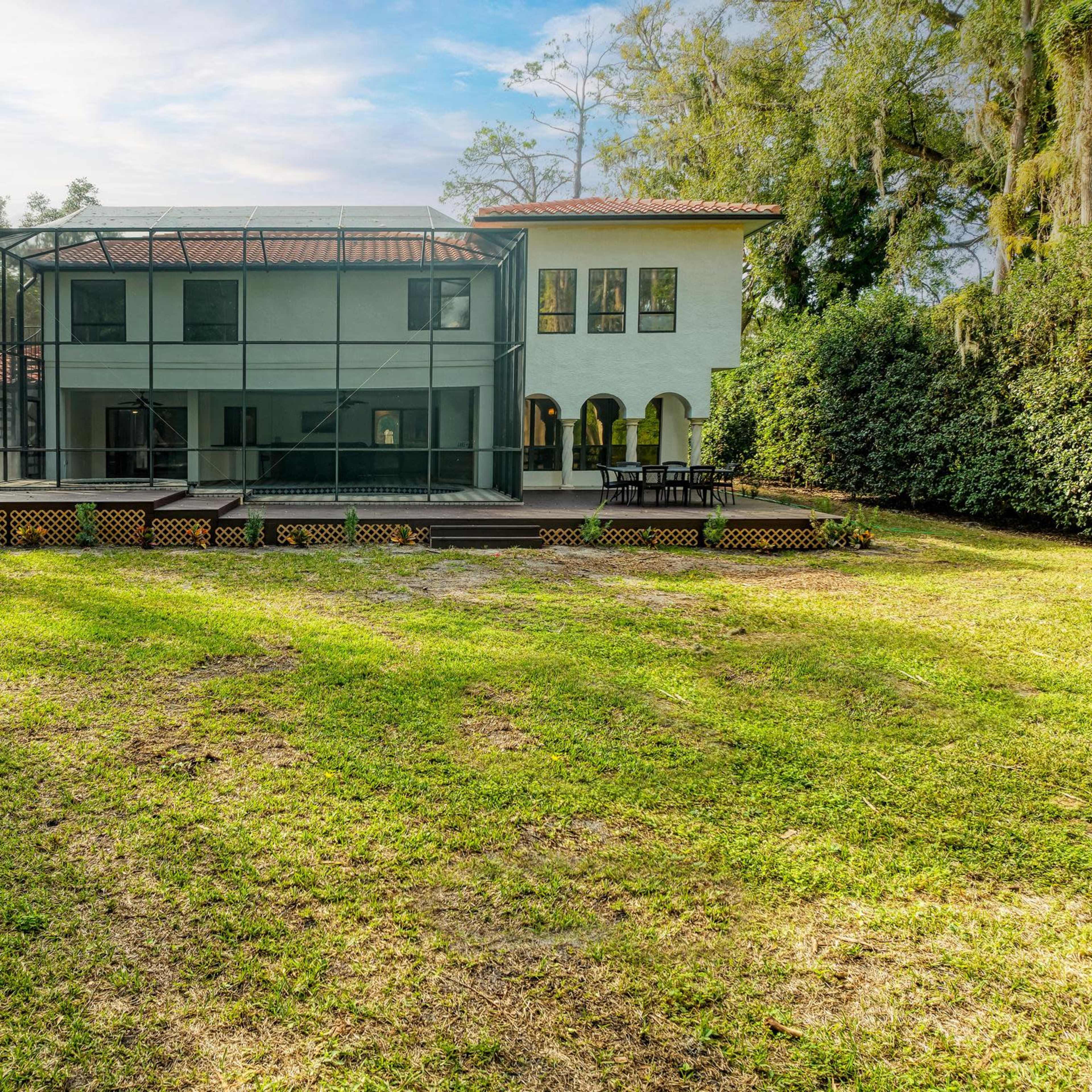 A two-story house with a large screened patio is surrounded by a grassy yard and trees.