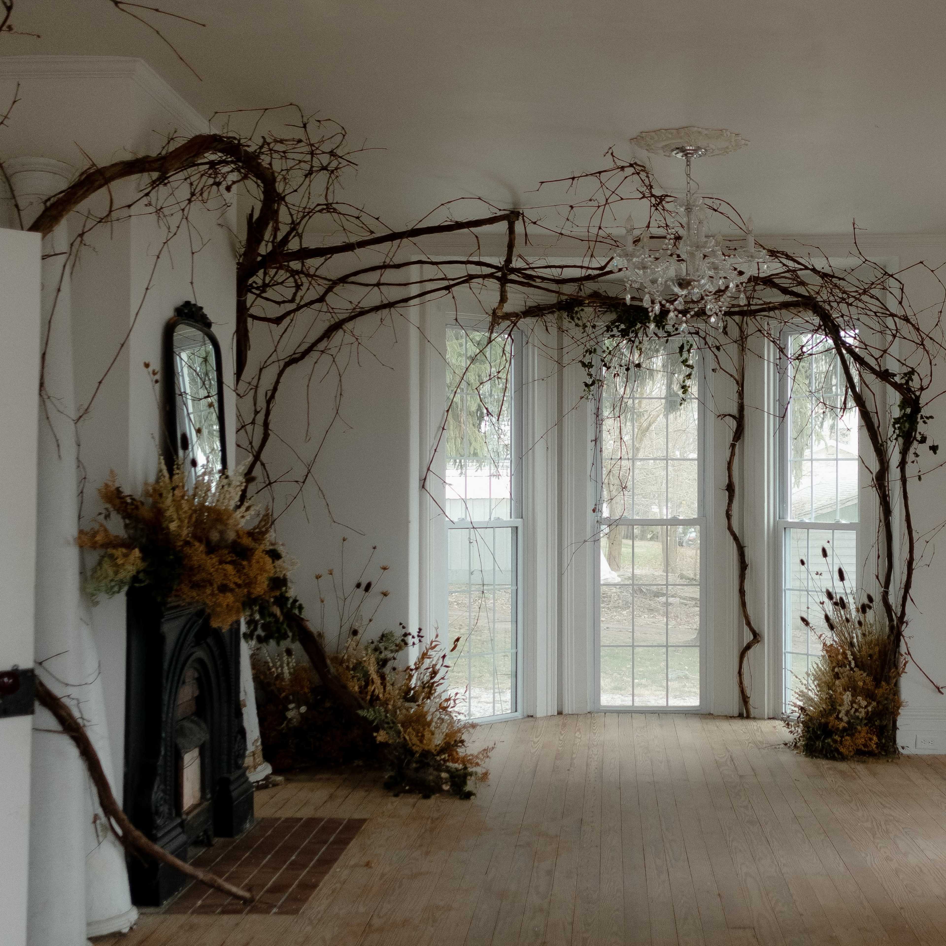 The room features large windows, a chandelier, and natural elements like branches and dried flowers decorating the walls and floor.