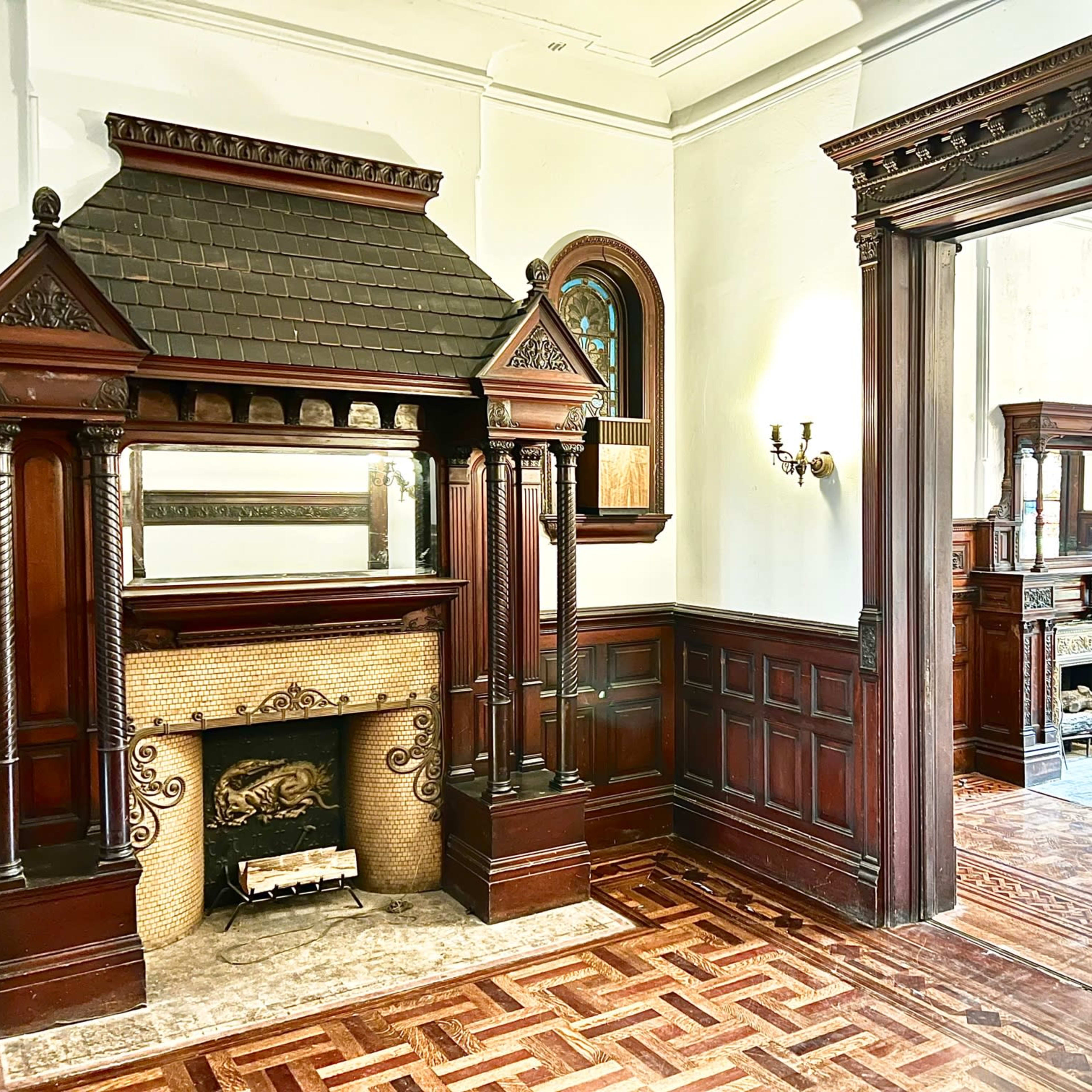 A vintage interior featuring ornate wooden paneling, intricate mantelpieces, and decorative details in a spacious room.