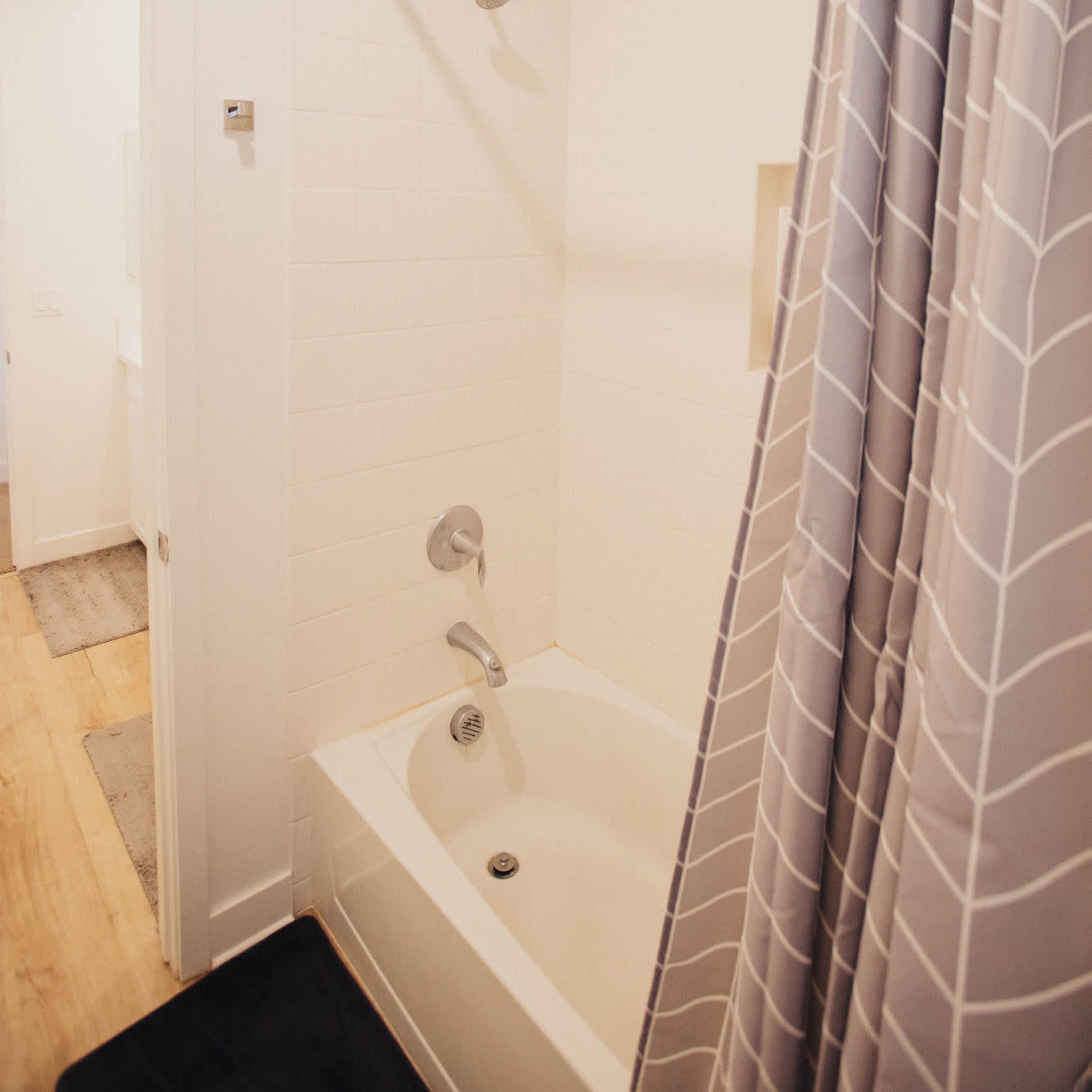 A bathroom featuring a bathtub with a shower curtain and a showerhead above it, adjacent to an open door leading to another room.