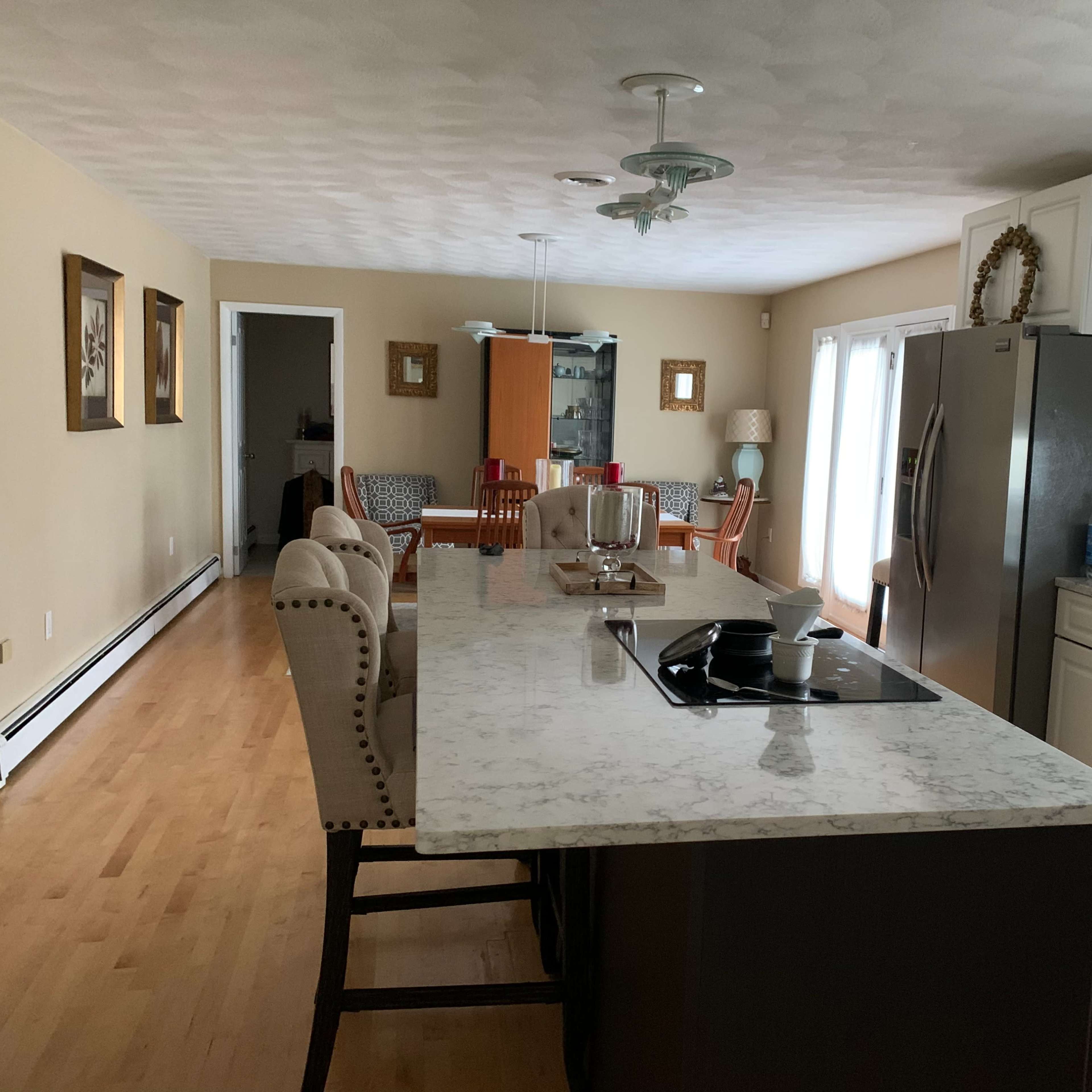 A spacious kitchen features a marble island, stainless steel appliances, and an open dining area with wooden furniture.