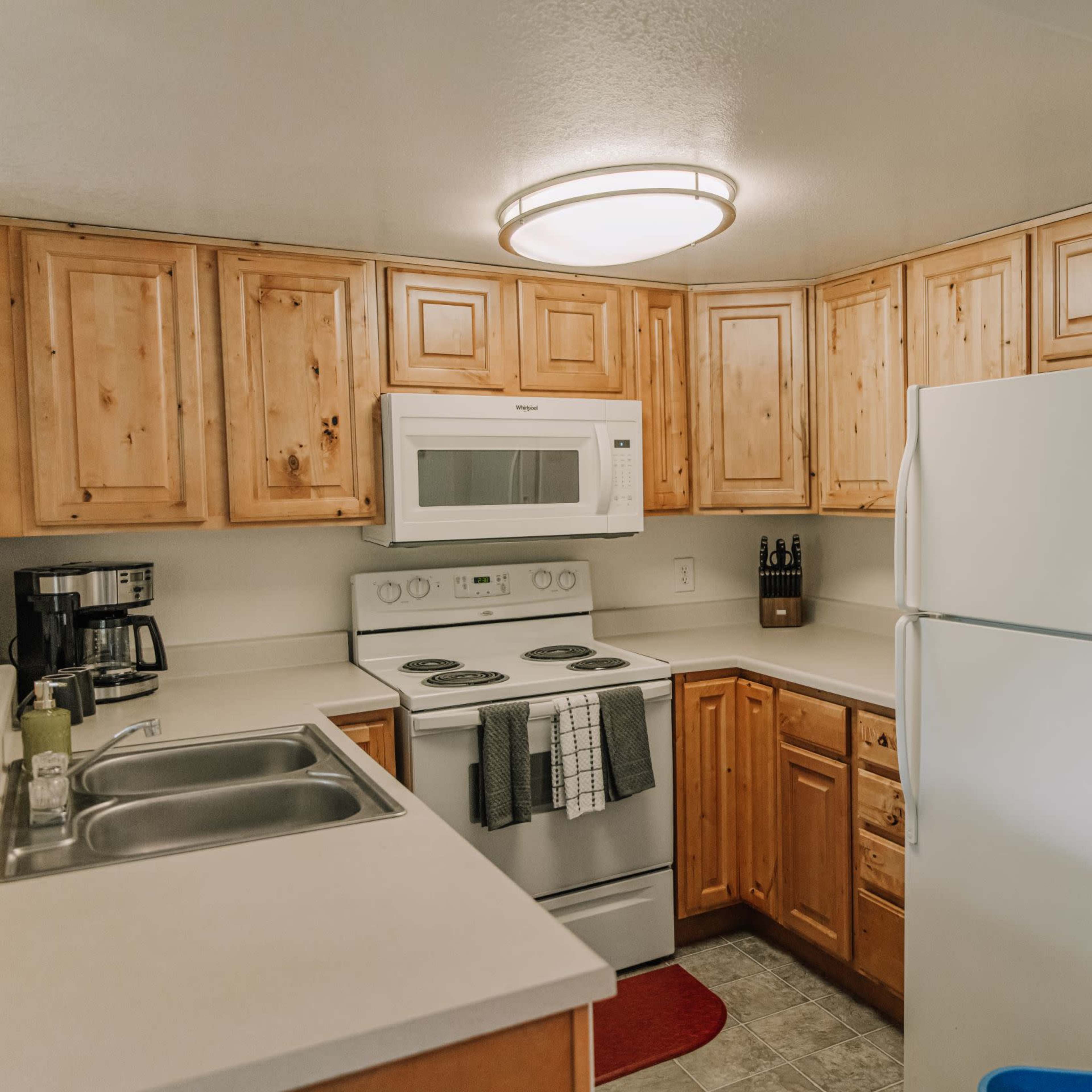 A small kitchen with wooden cabinets, stainless steel appliances, and a white countertop.