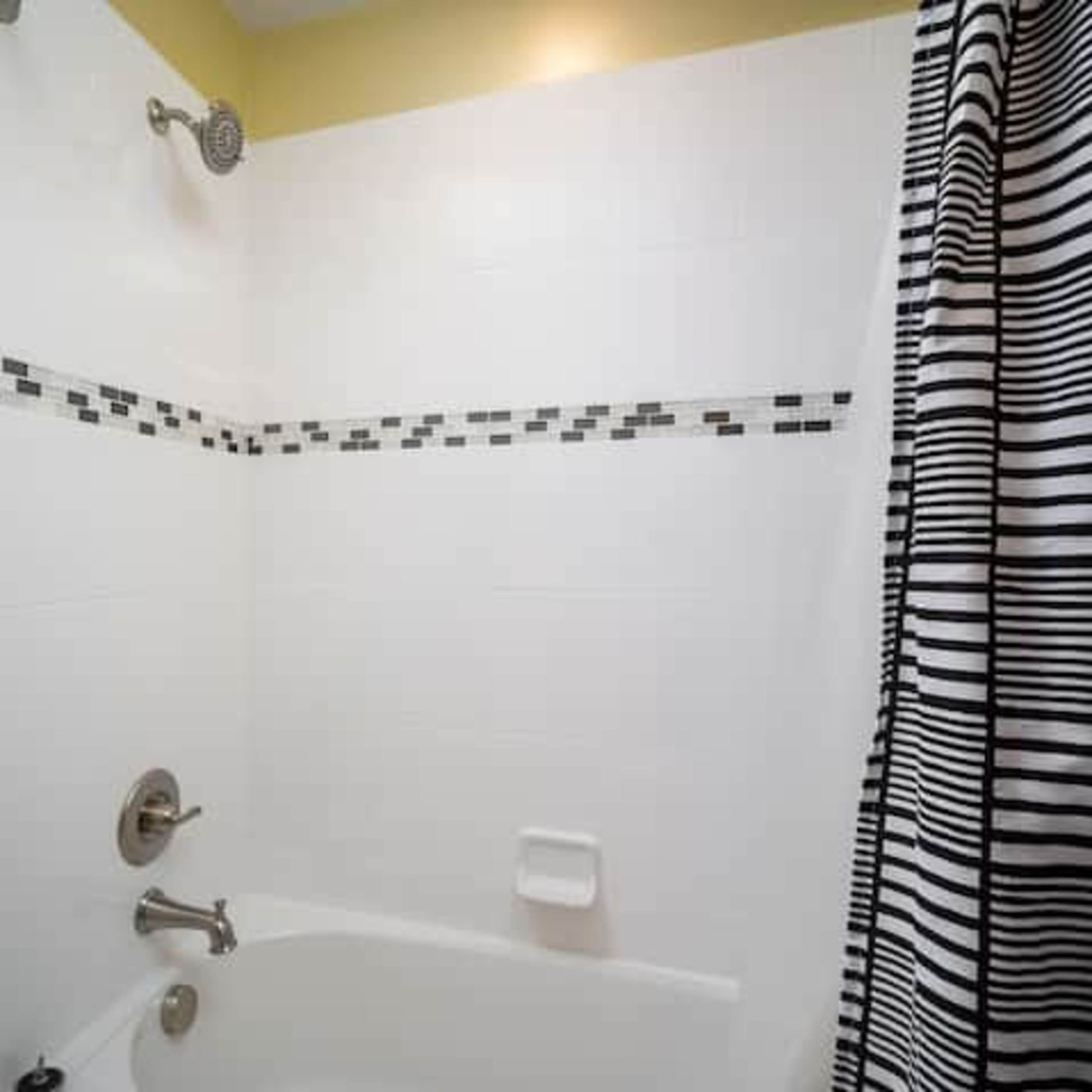 A bathroom with a white tiled shower area featuring a black and white striped shower curtain.