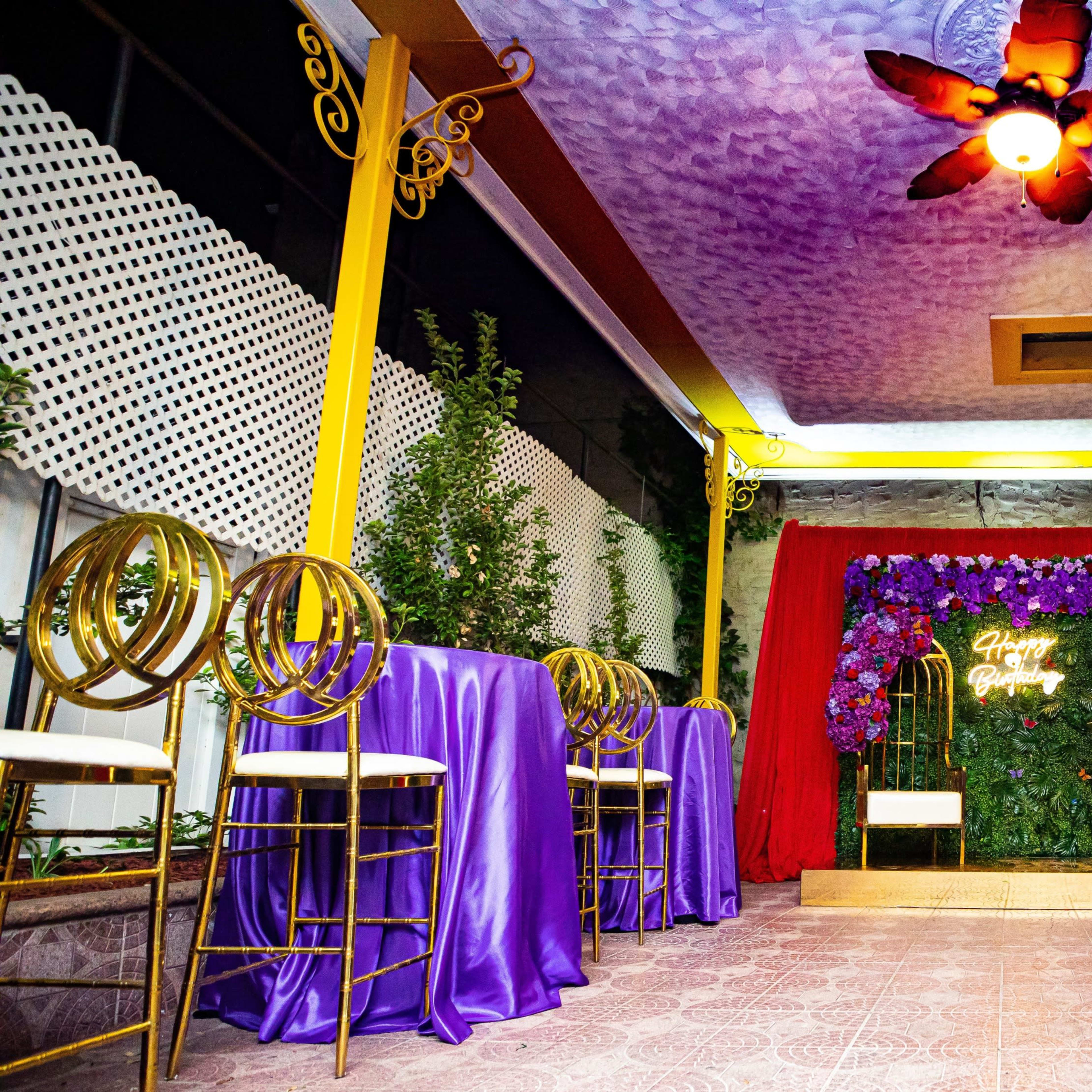 An event space decorated with purple tablecloths, gold accents, and a floral backdrop for a celebration.