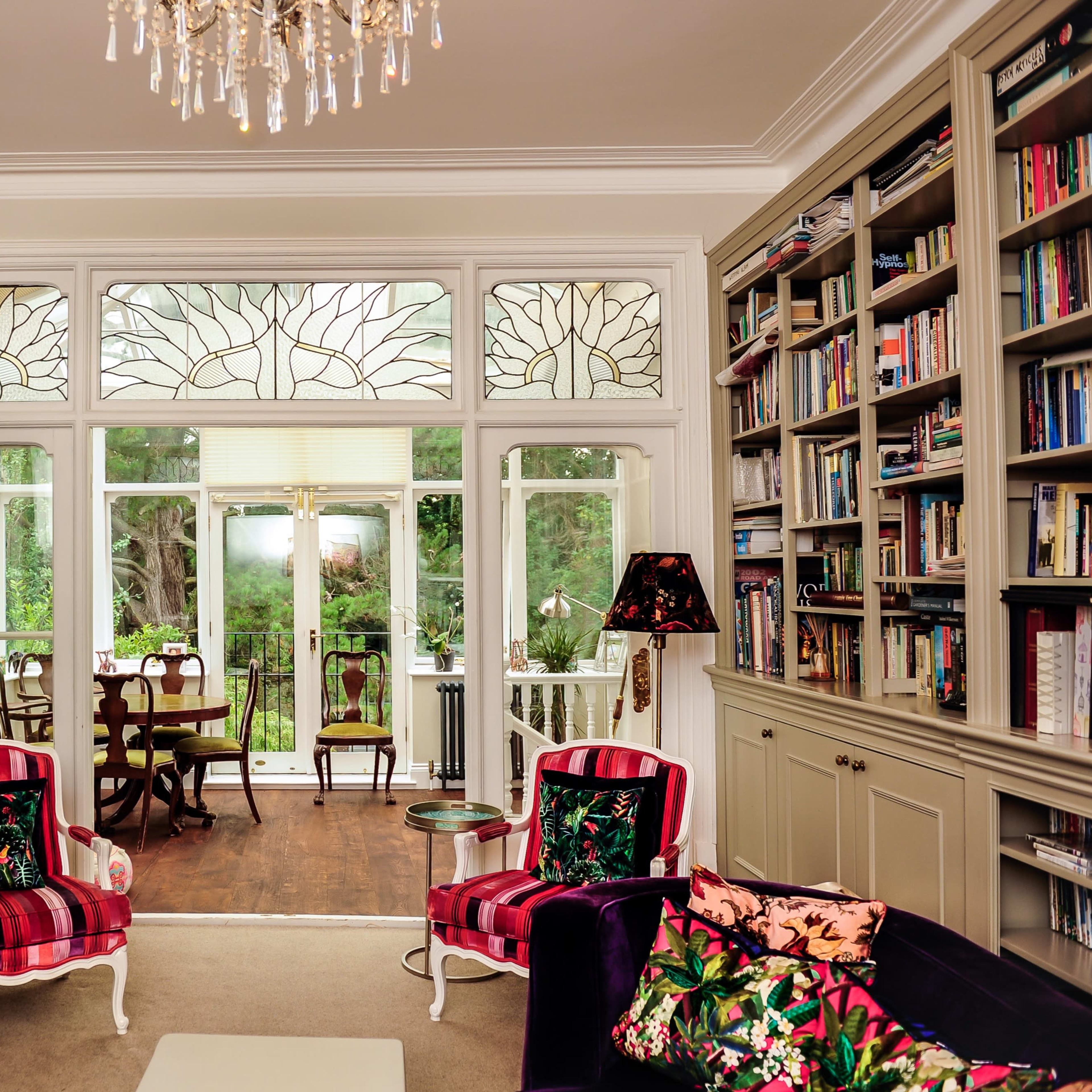 The room features two pink chairs with floral patterns facing a large window with decorative glass, overlooking a garden space.