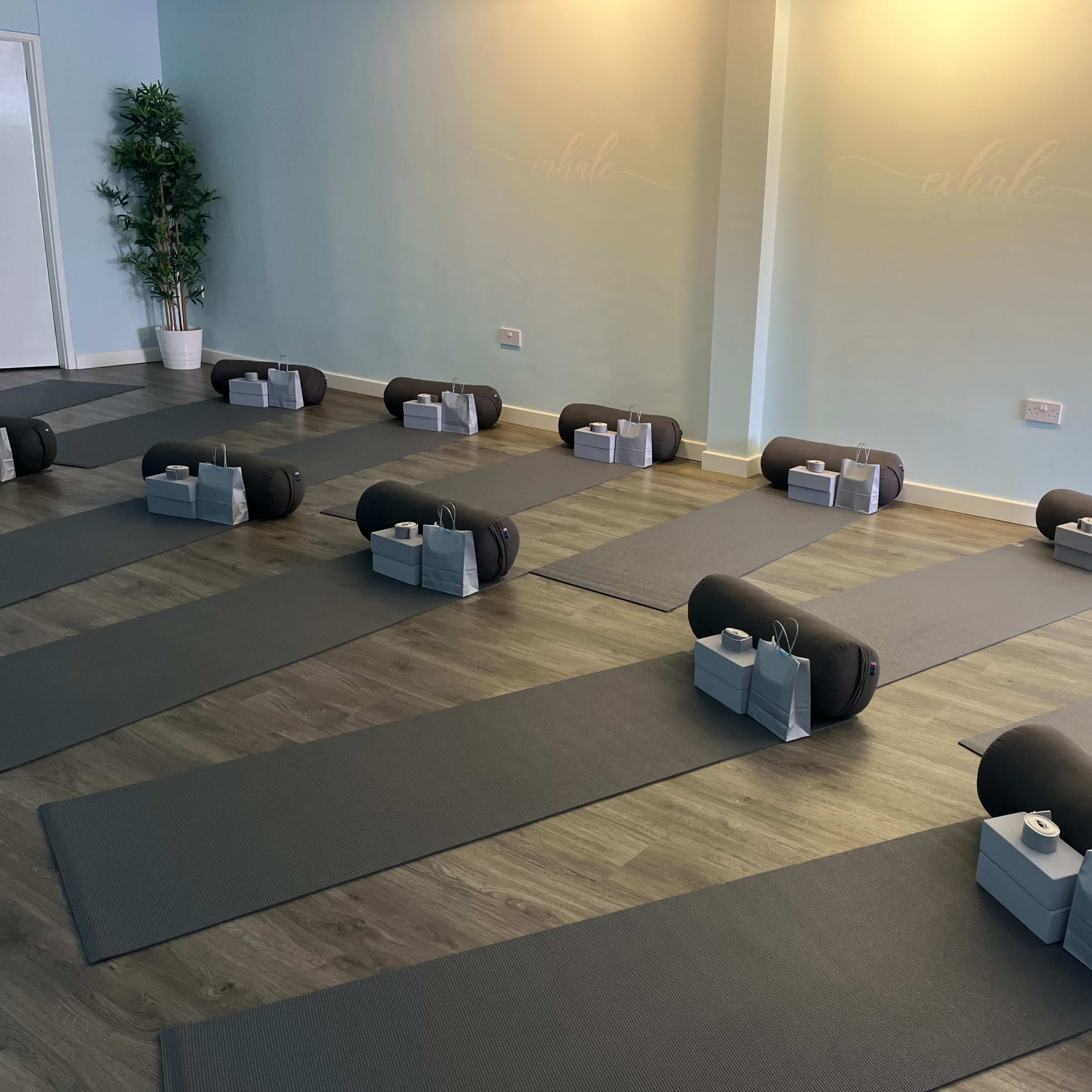 A neatly arranged yoga studio with several exercise mats laid out in rows, each accompanied by a bolster and a water bottle.