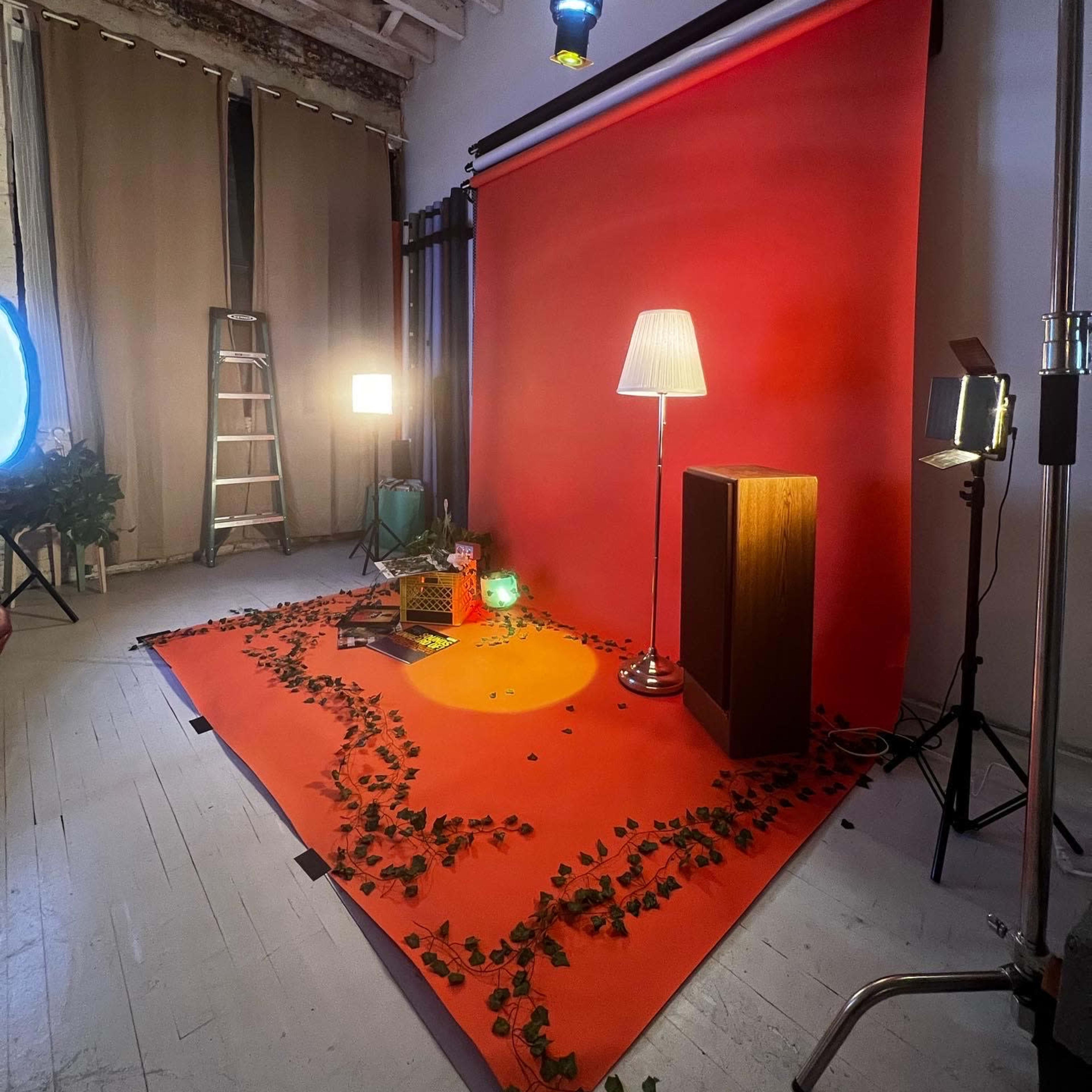 A photo studio set up with a red backdrop, a lamp, a wooden cabinet, and scattered leaves on the floor.