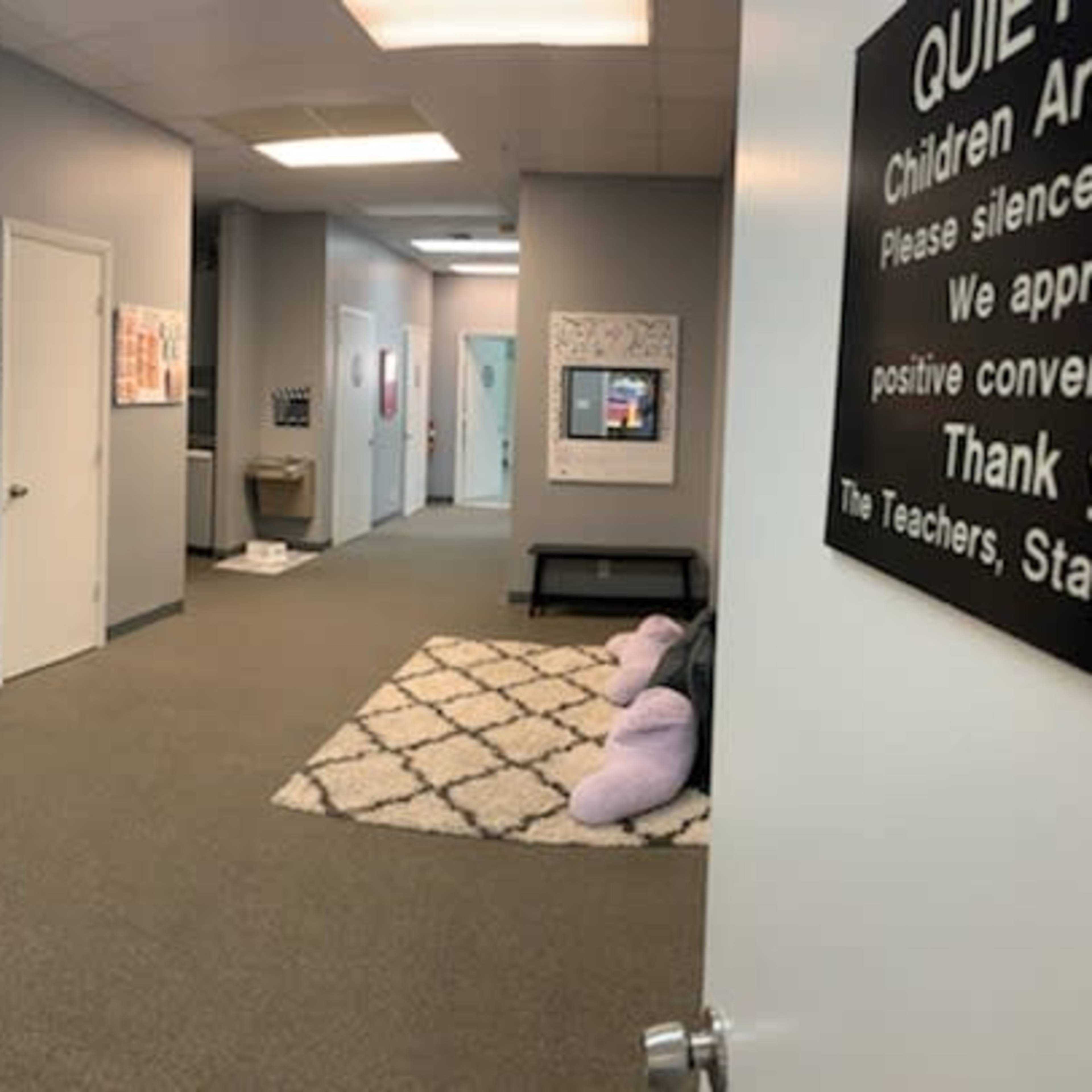 A hallway in a facility featuring lockers on the left, a carpeted floor, and several doors leading to different rooms.