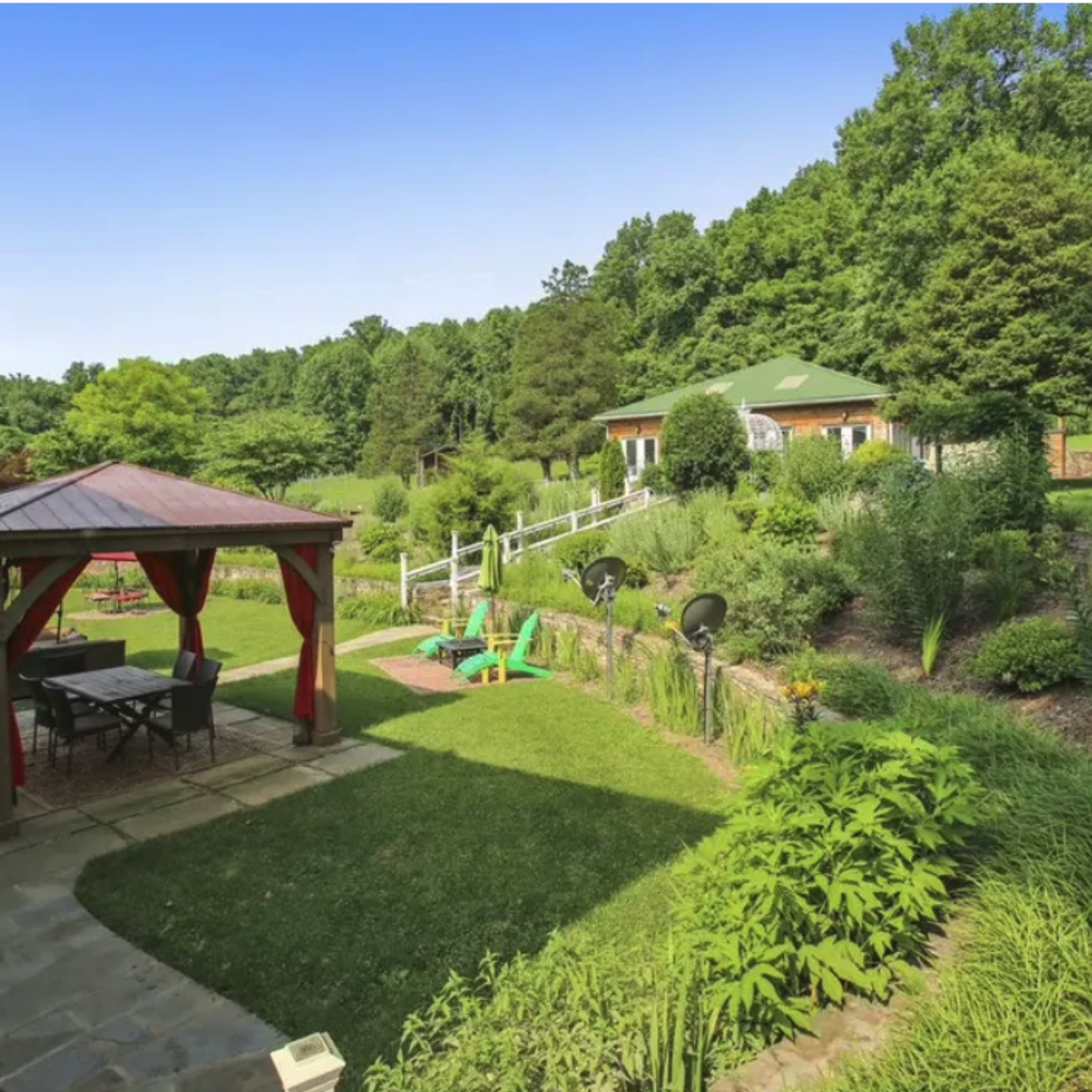 A landscaped garden with a gazebo, outdoor seating, and a house surrounded by greenery.