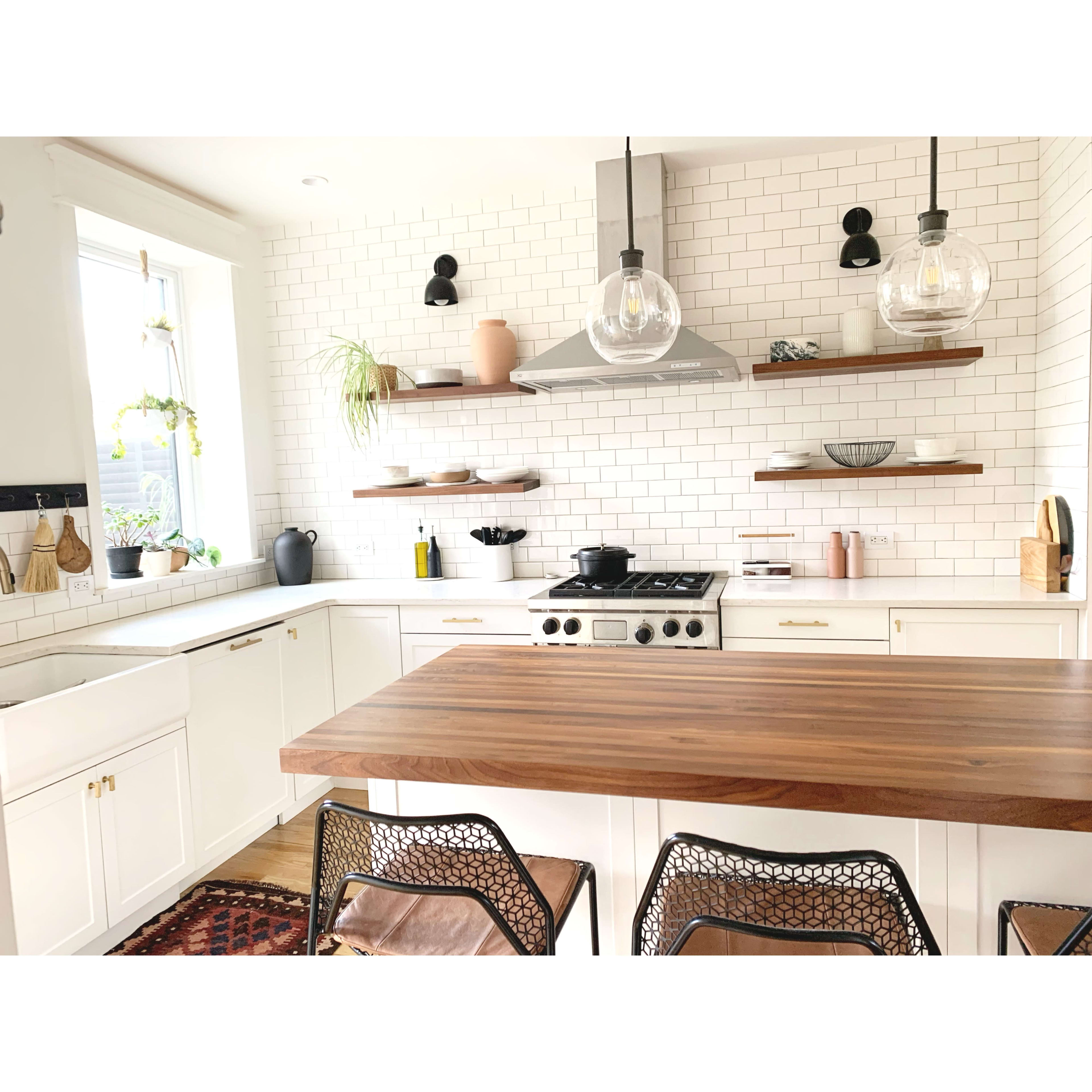 A modern kitchen features white cabinets, a large wooden island, and open shelves displaying various kitchenware against a tiled backsplash.