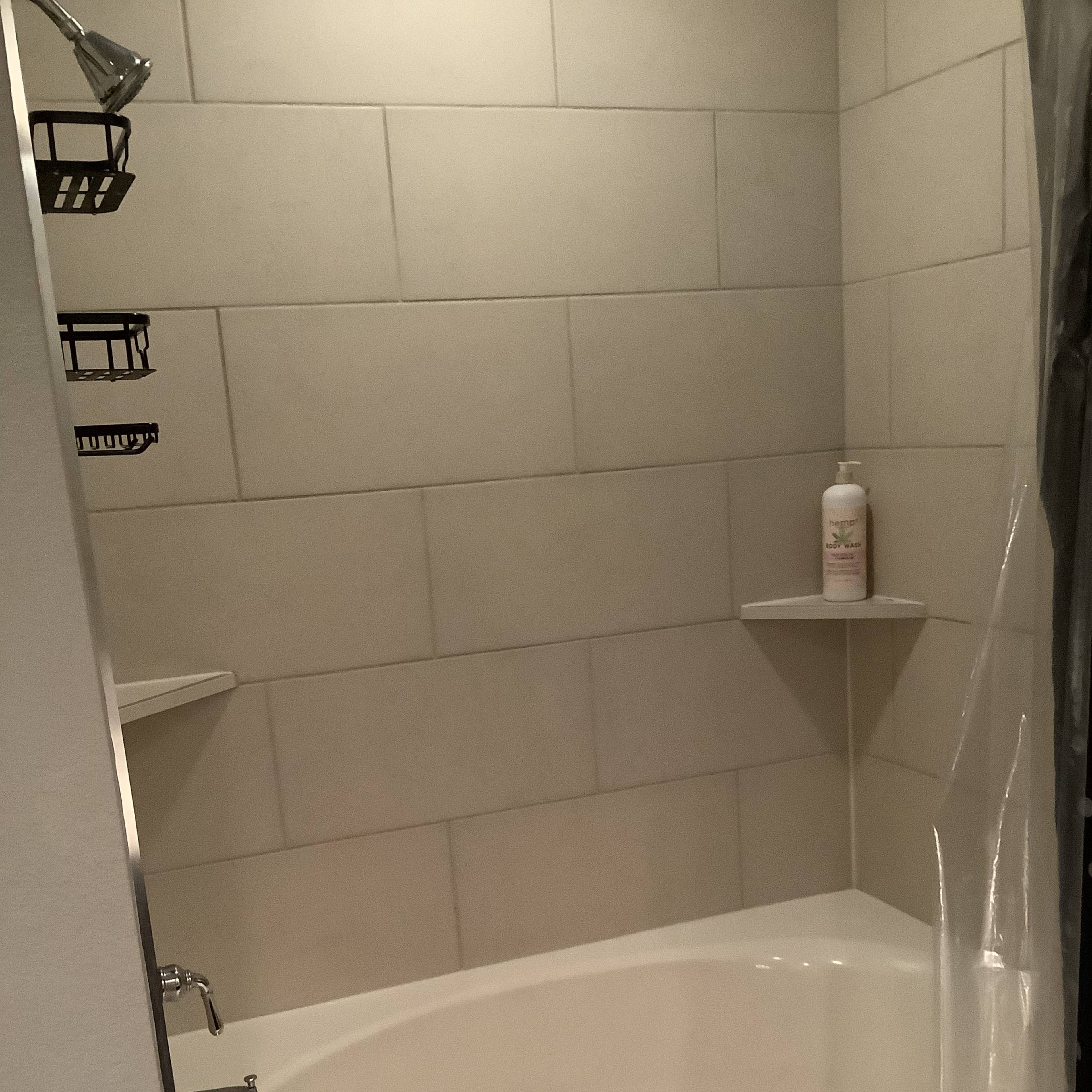 A clean, tiled shower area with a bathtub, two corner shelves, and a bottle of shampoo.
