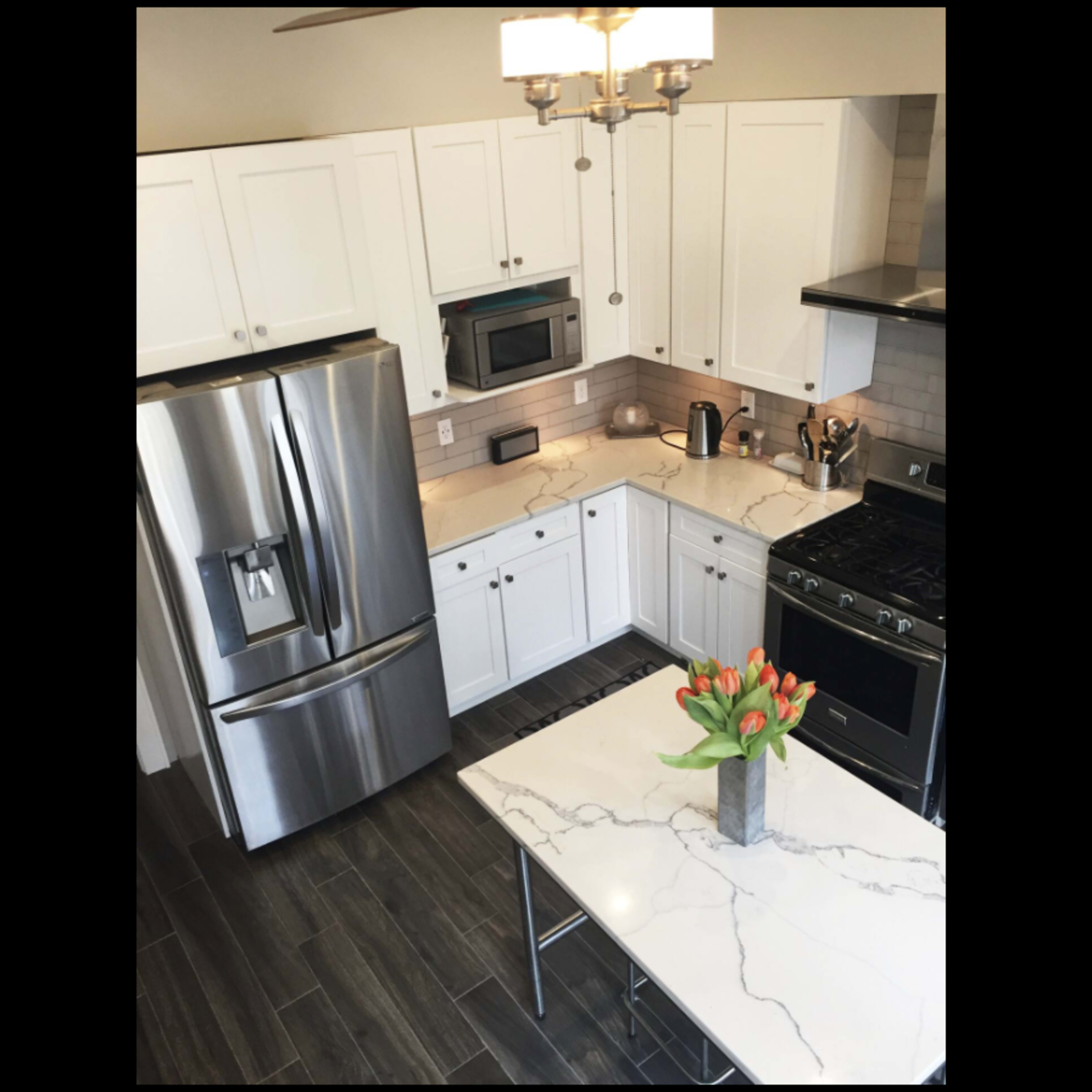 A modern kitchen features stainless steel appliances, white cabinets, and a marble-topped island with a vase of tulips.