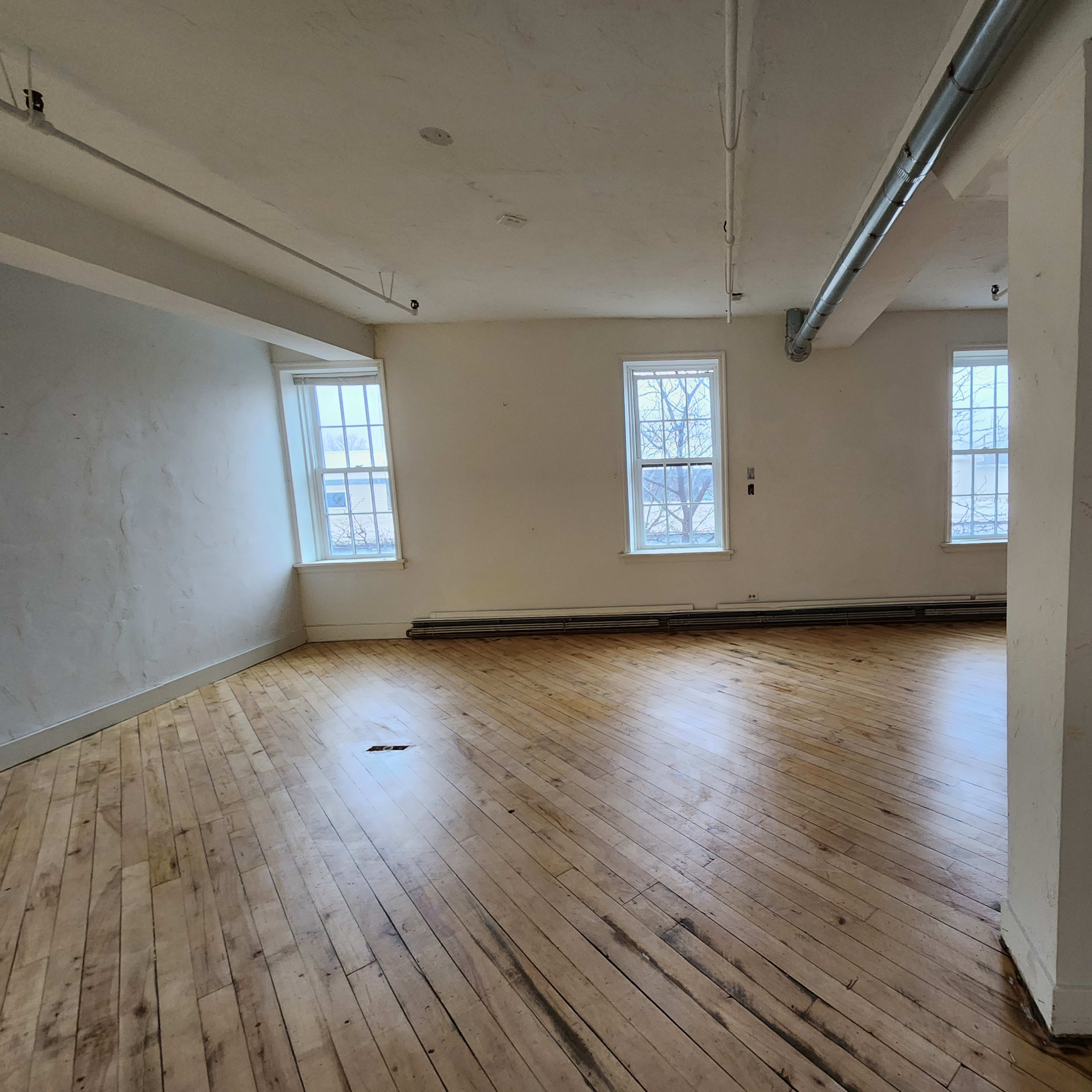 An empty room with wooden floors, white walls, and two windows on one side.