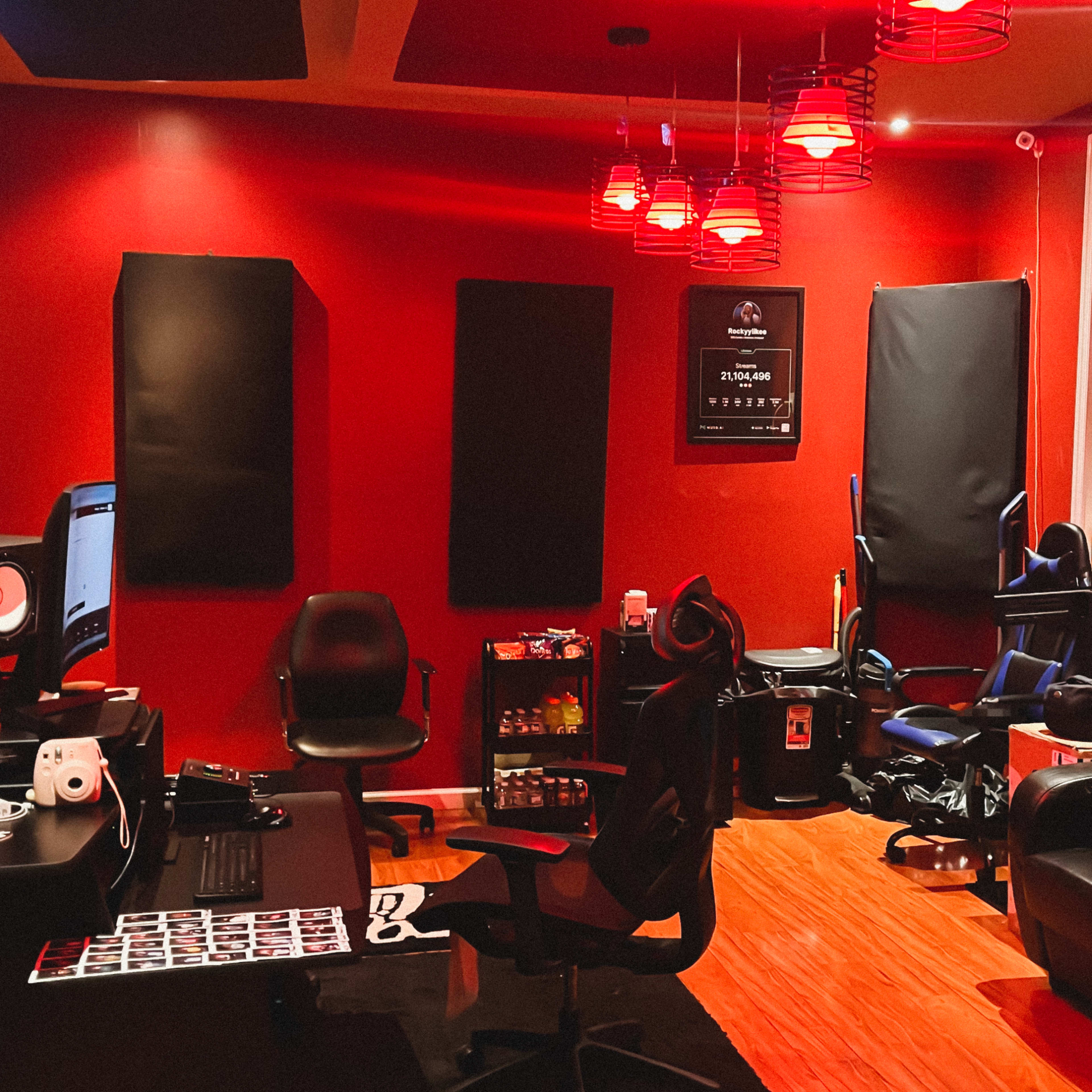 A recording studio with red walls, black soundproofing panels, multiple chairs, and a desk equipped with music production equipment.