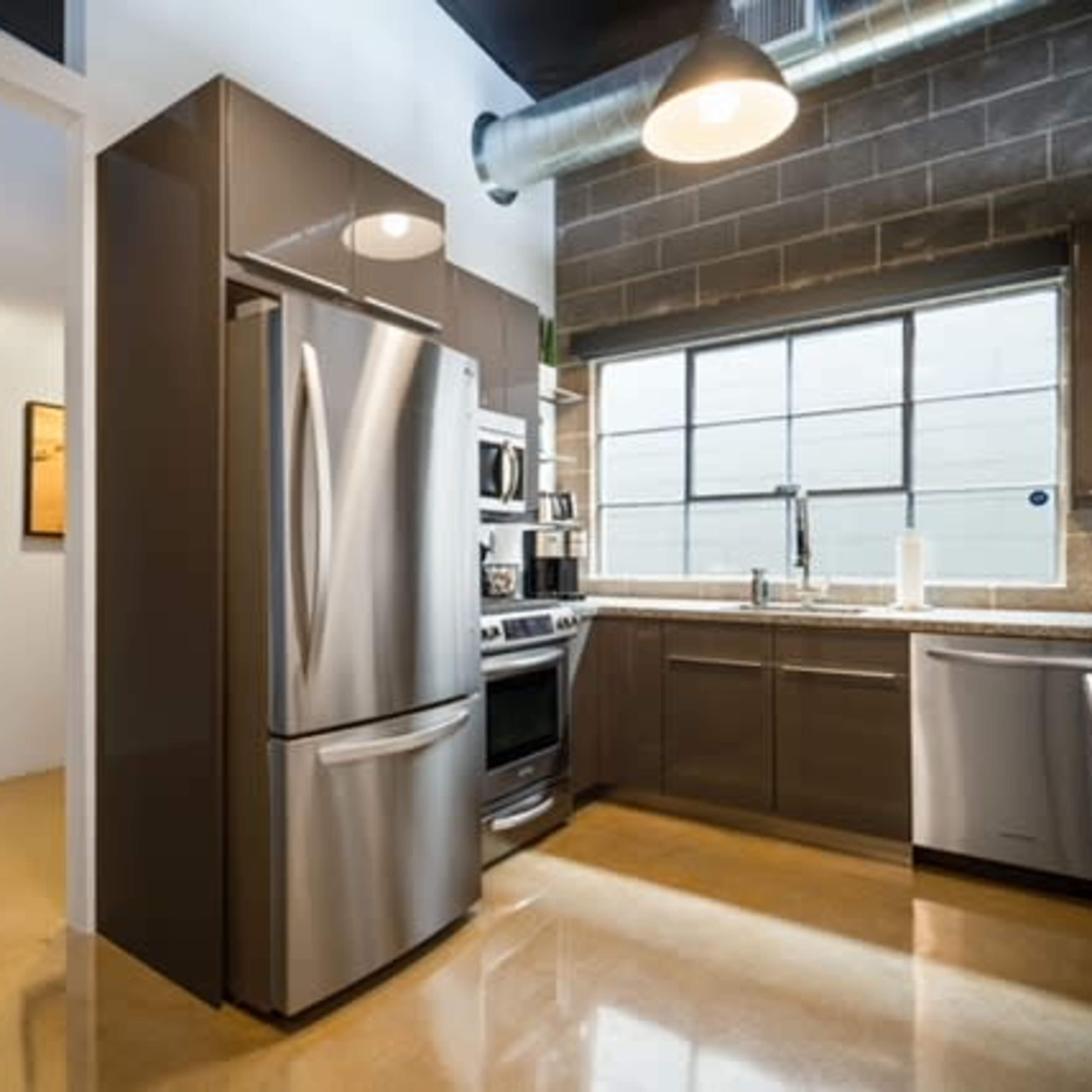 A modern kitchen with stainless steel appliances, including a refrigerator and an oven, along with dark cabinetry and a large window.
