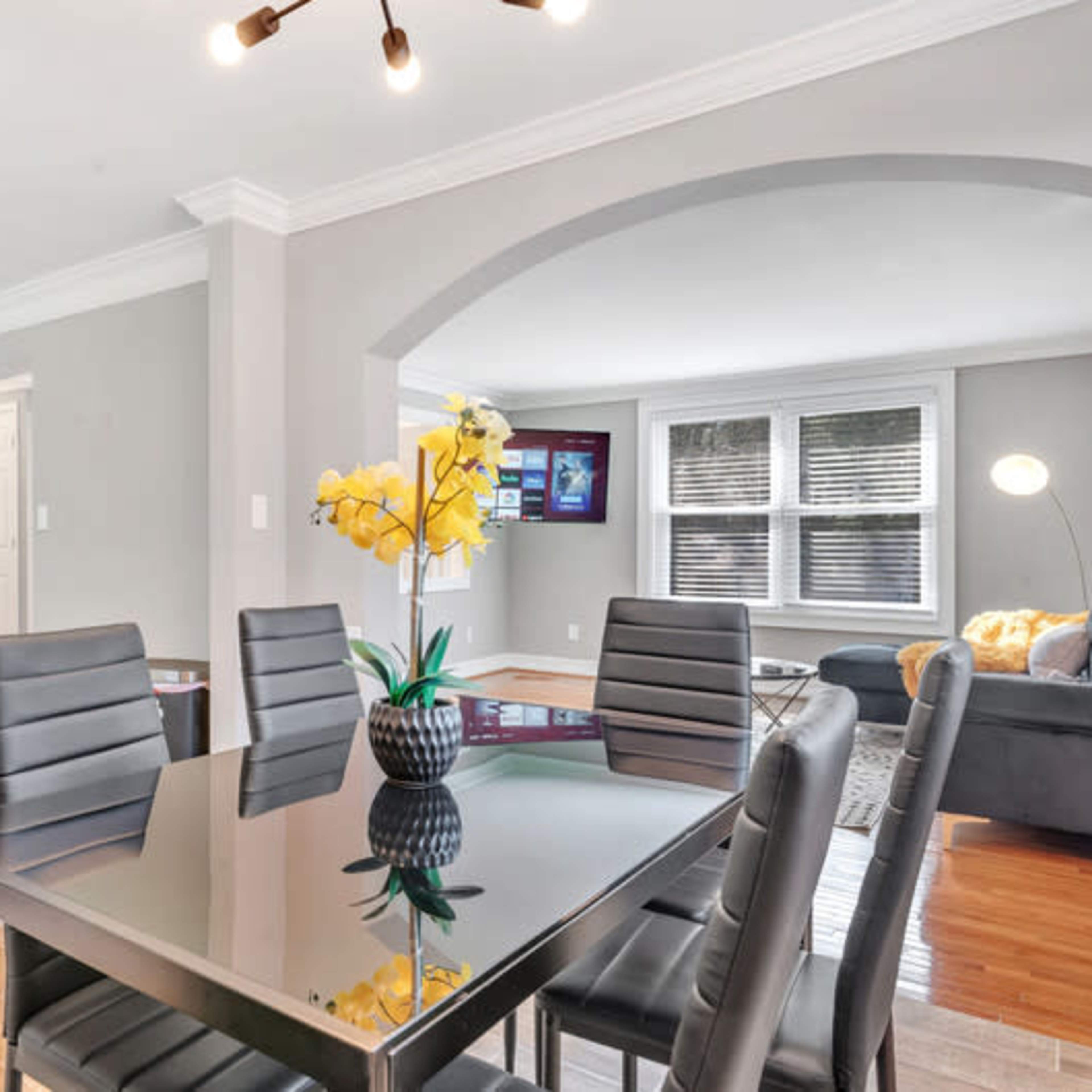 A modern dining area with a glass table and black chairs adjacent to a kitchen featuring stainless steel appliances.