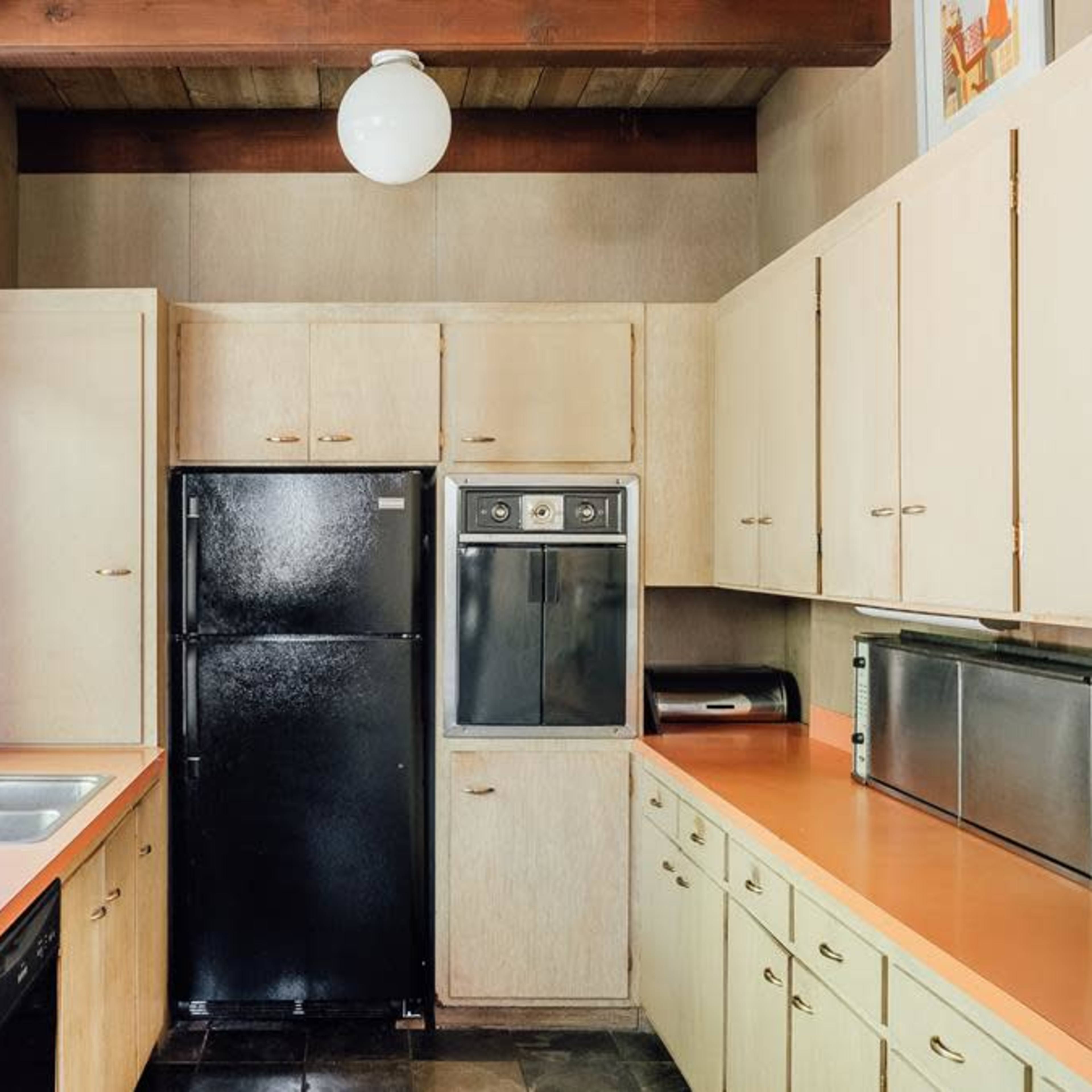 A modern kitchen with wooden beams, light-colored cabinetry, and appliances, including a black refrigerator and a stainless steel microwave.