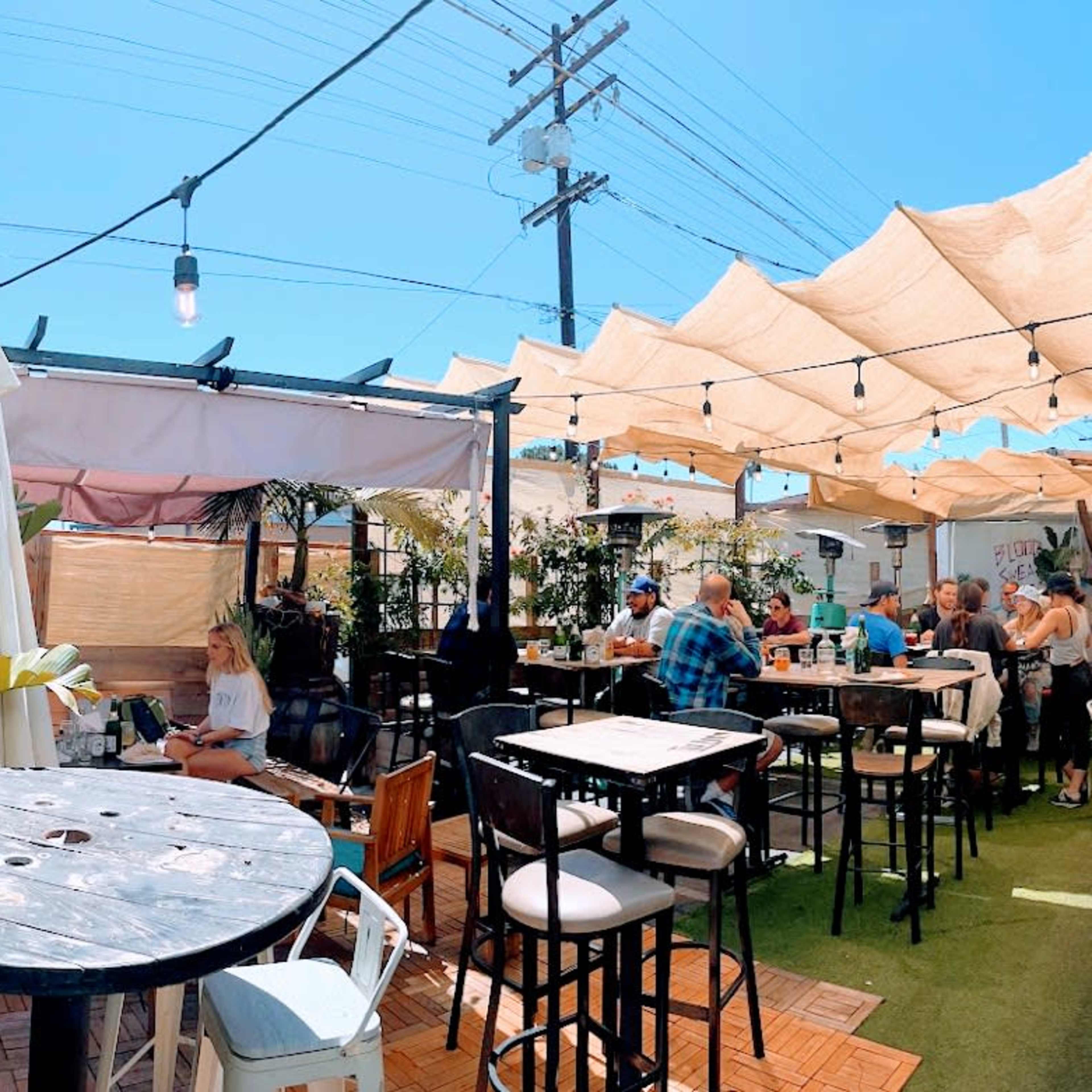 A vibrant outdoor seating area of a restaurant, with patrons dining under shaded canopies and string lights.