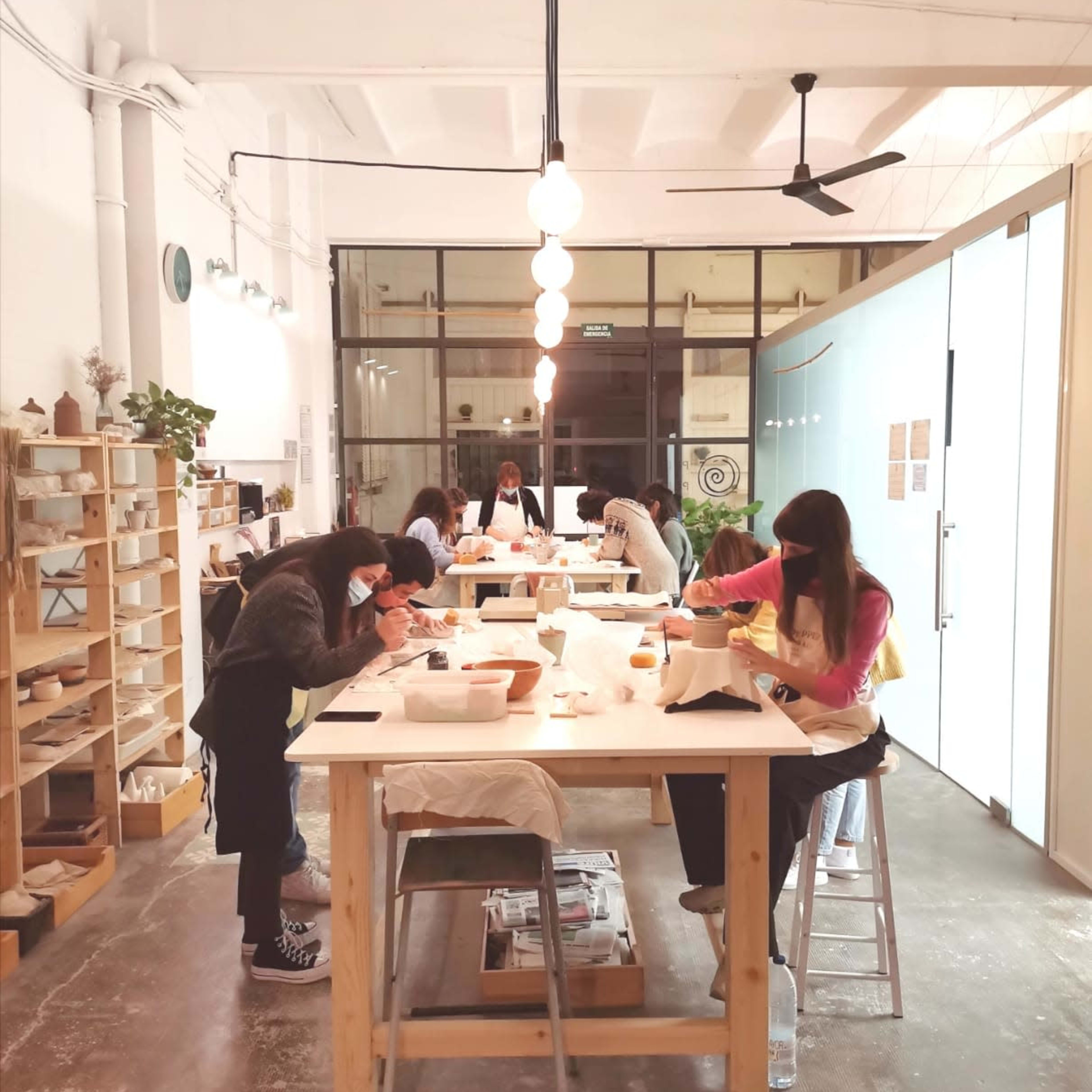 A group of individuals is engaged in pottery crafting at a long table in a bright, minimalist studio.