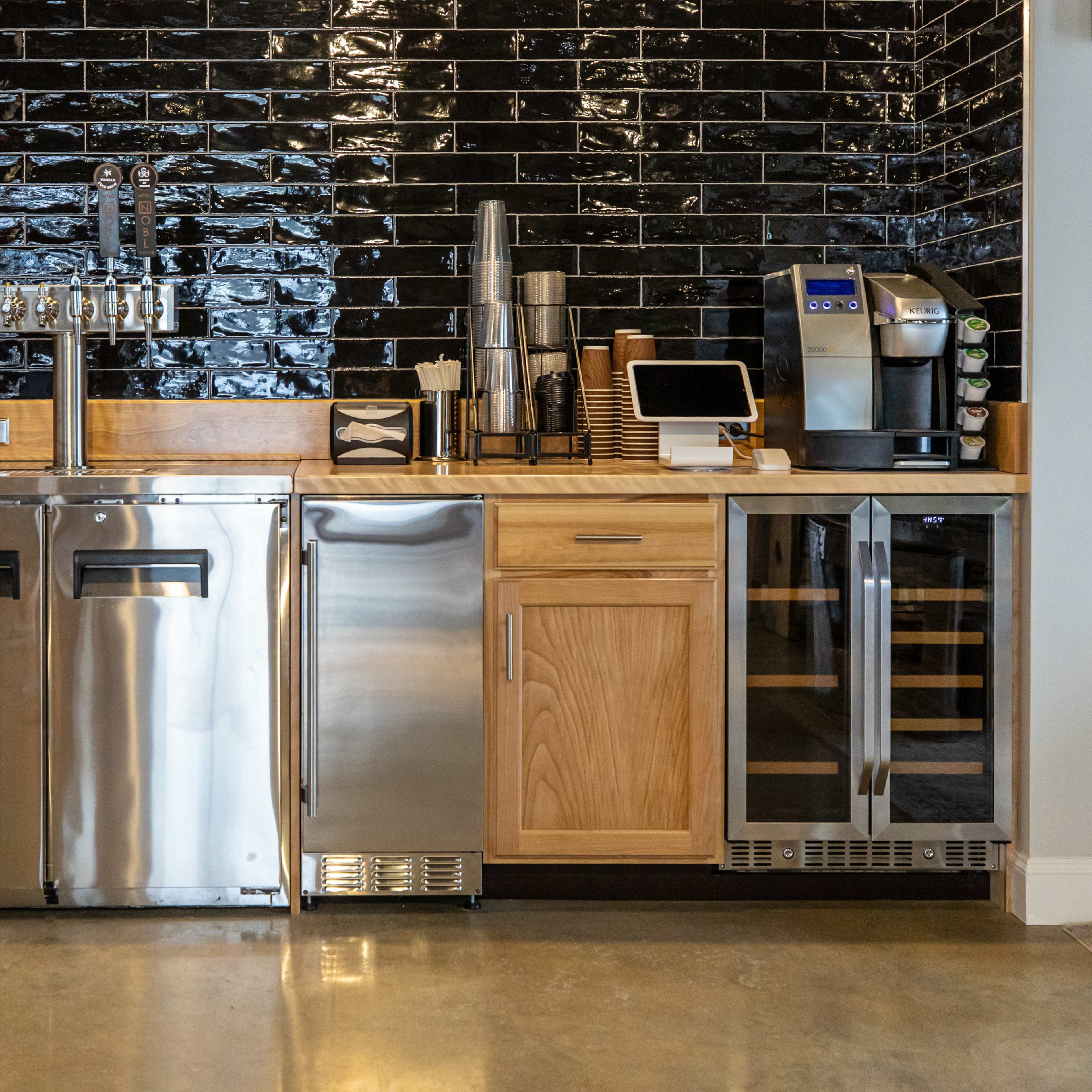 A modern kitchen bar with stainless steel appliances, a wooden countertop, and a black tiled backsplash.