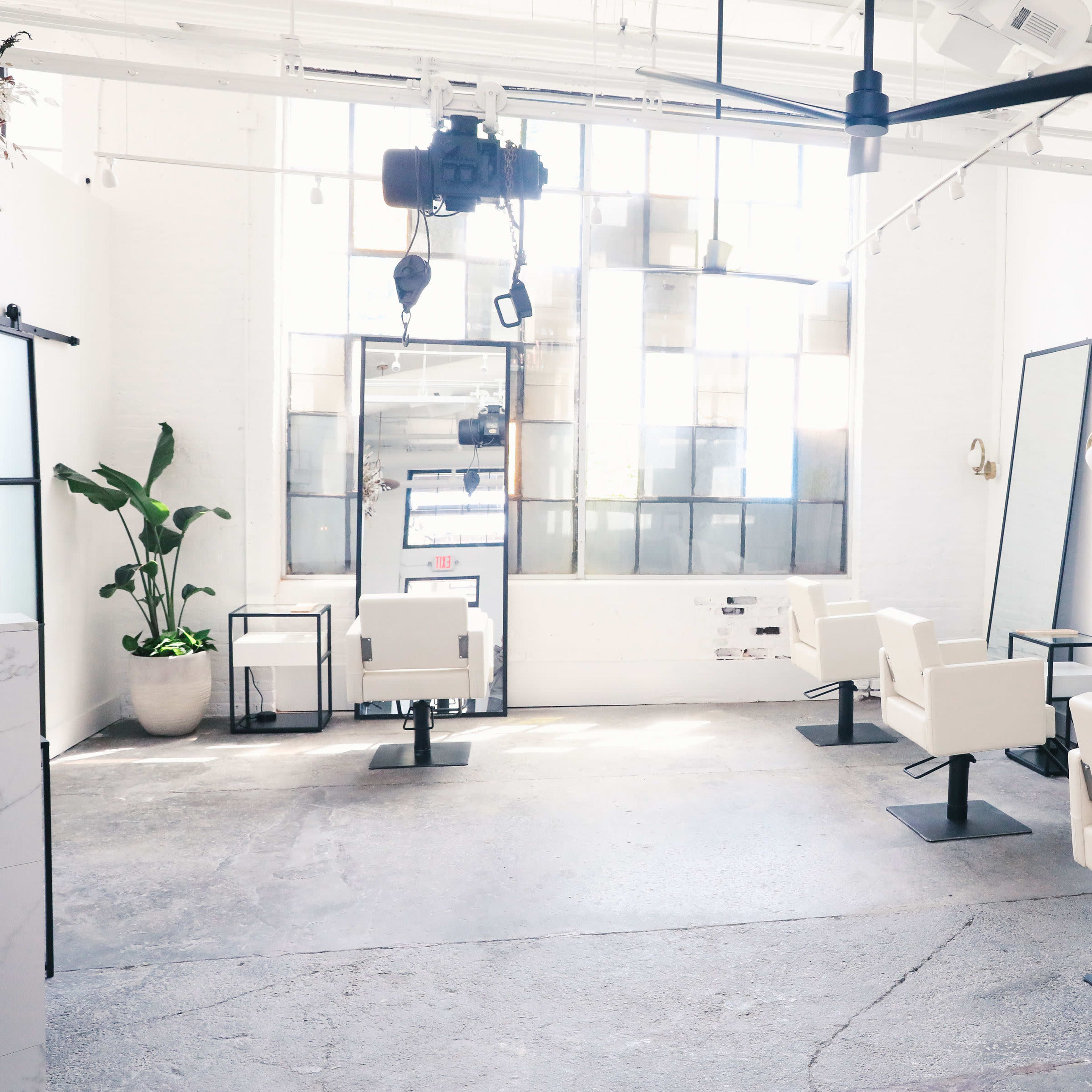 A bright, minimalist salon with white walls, large mirrors, and several hairdressing chairs arranged in a spacious layout.