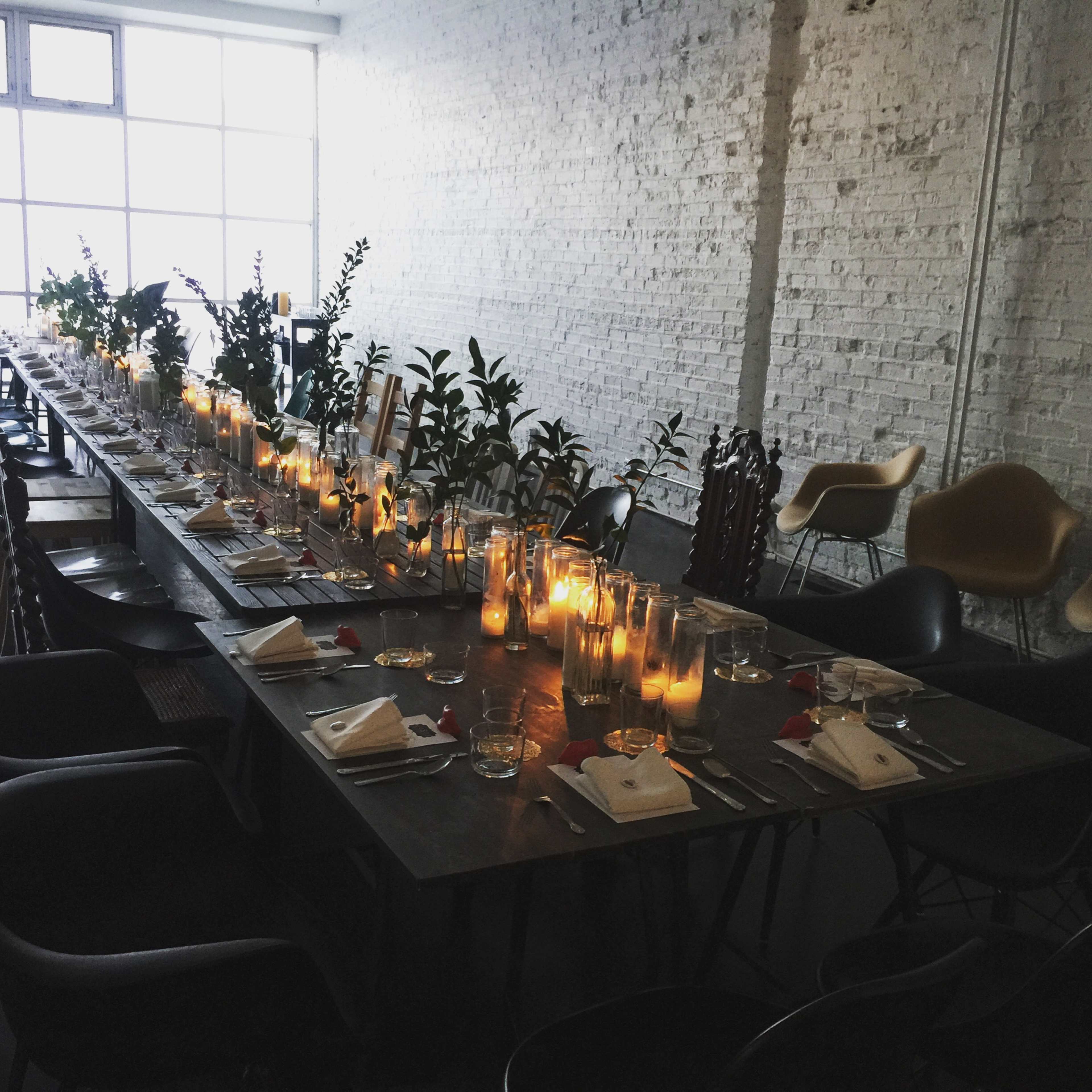 A long dining table is set with candles and greenery in a well-lit, minimalistic room.