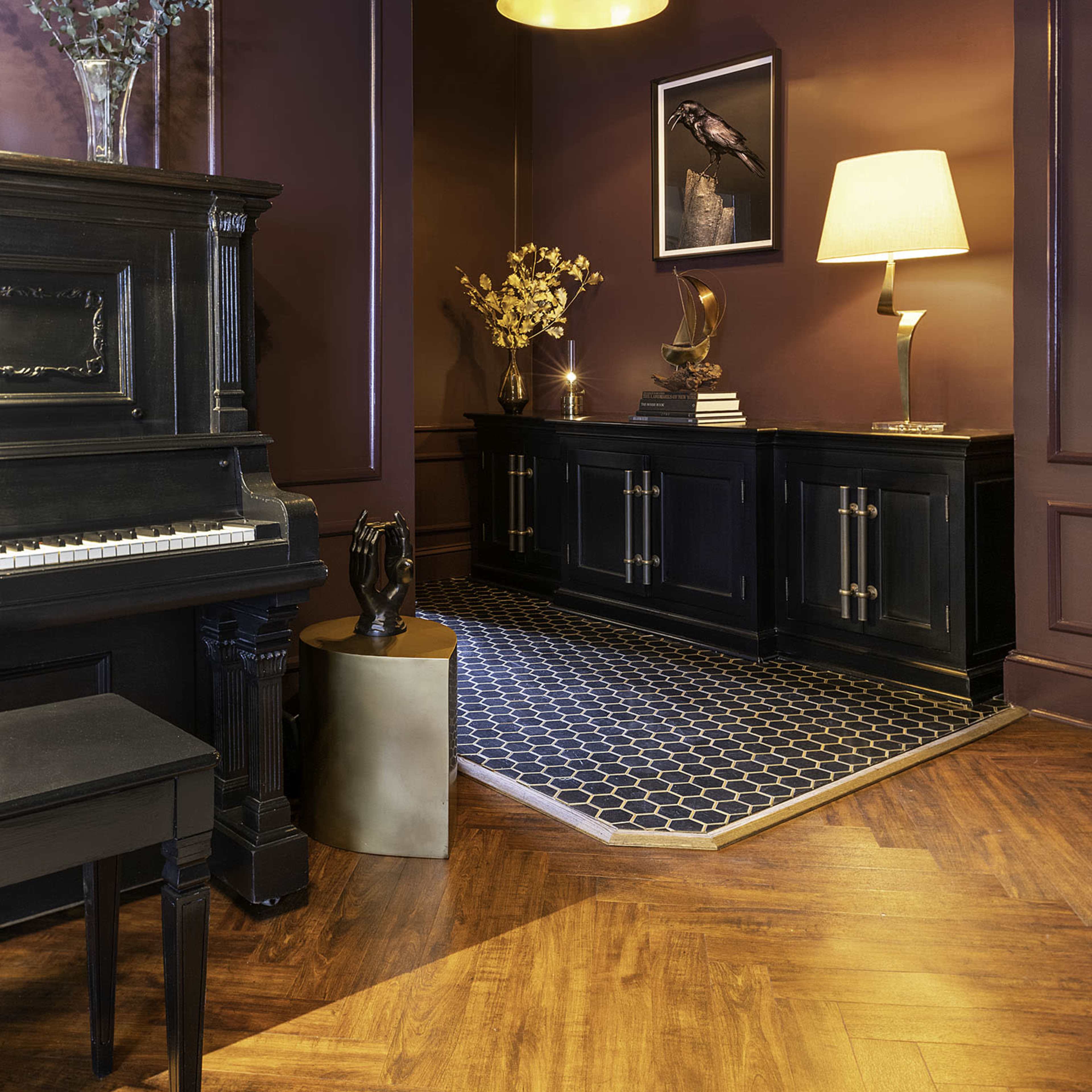A darkly painted corner features a piano, a wooden cabinet, a lamp, and decorative items on a patterned rug.