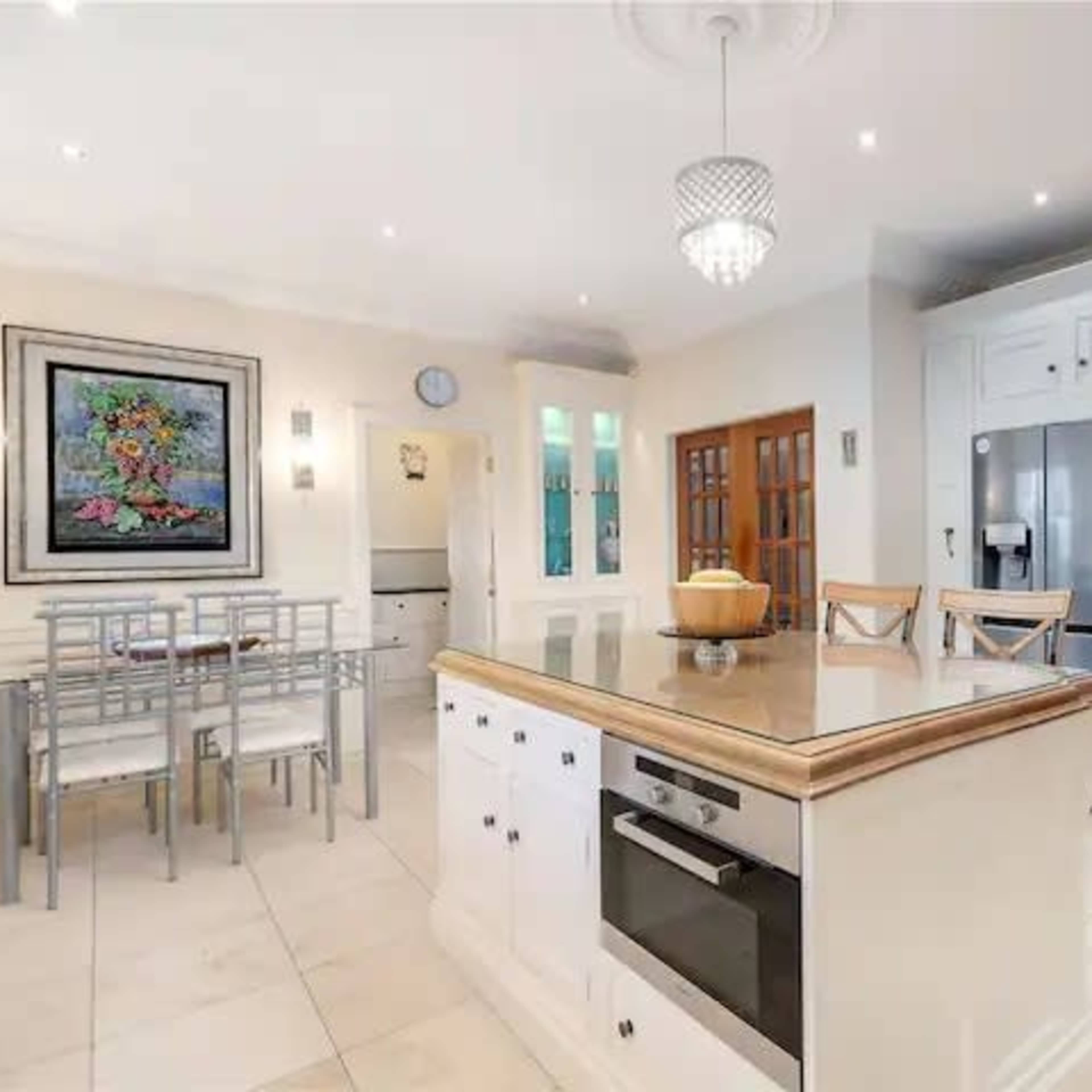 A modern kitchen featuring white cabinetry, a large island with a countertop, stainless steel appliances, and a small dining area with metal chairs.