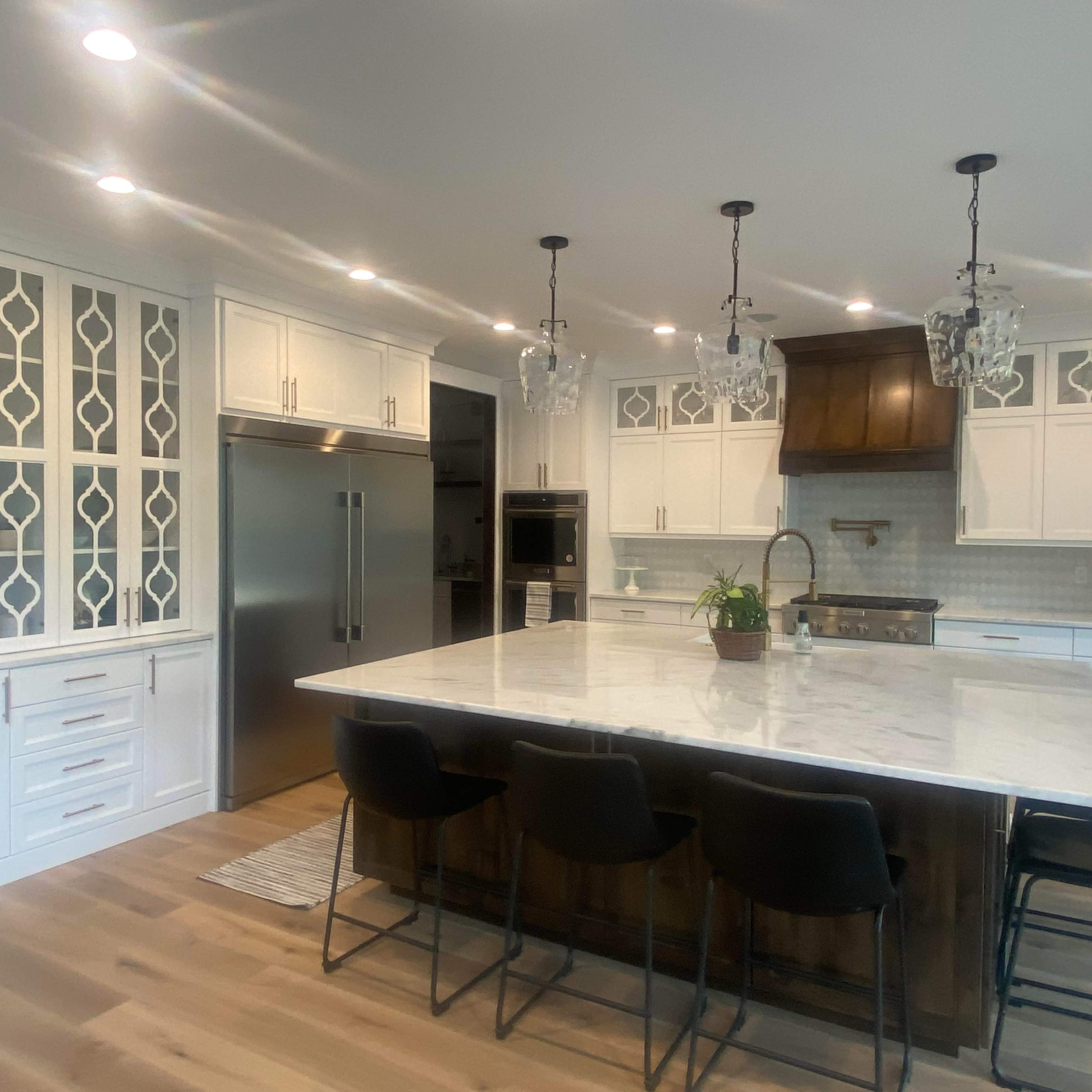 A modern kitchen featuring a large marble island, white cabinetry, and pendant lighting above.