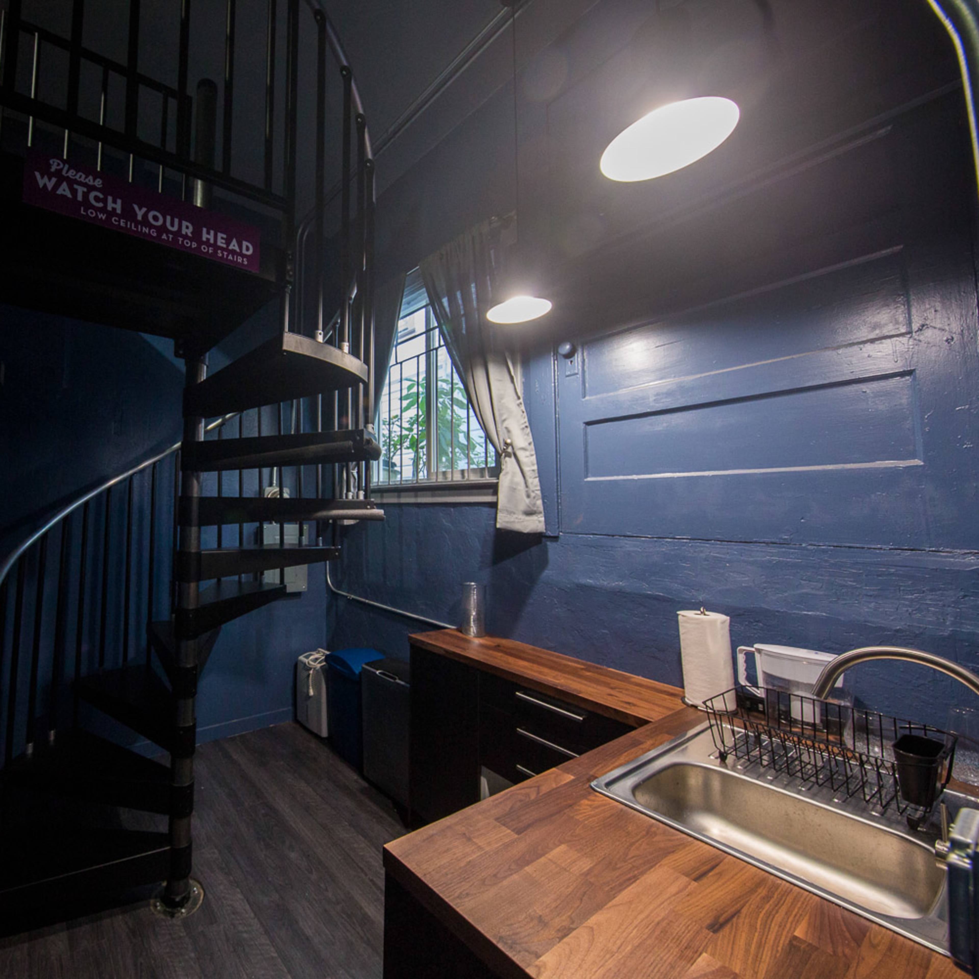 A small room featuring a spiral staircase, a kitchen area with wooden countertops, and blue painted walls.