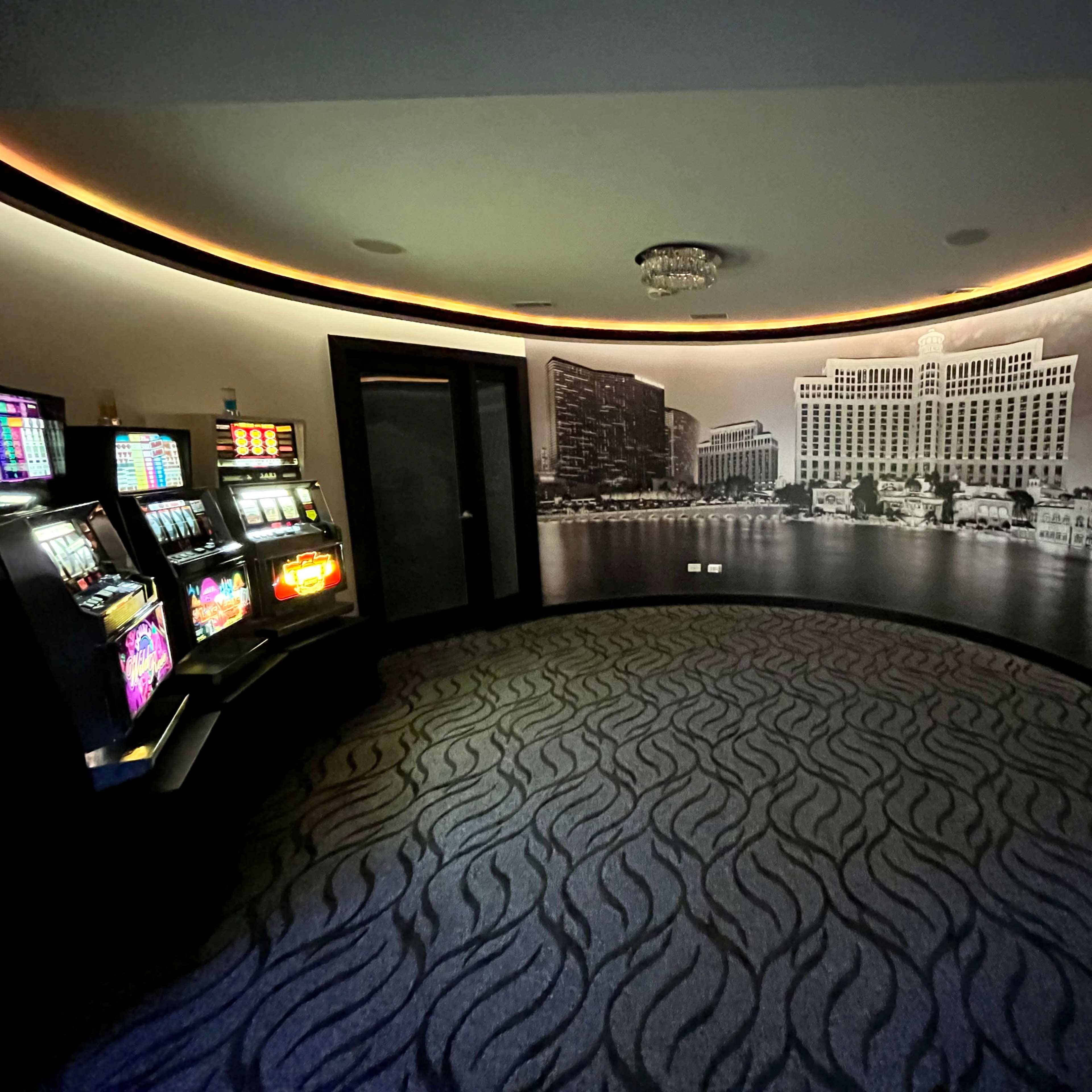A dimly lit gaming area featuring slot machines alongside a large black-and-white mural of a waterfront hotel.