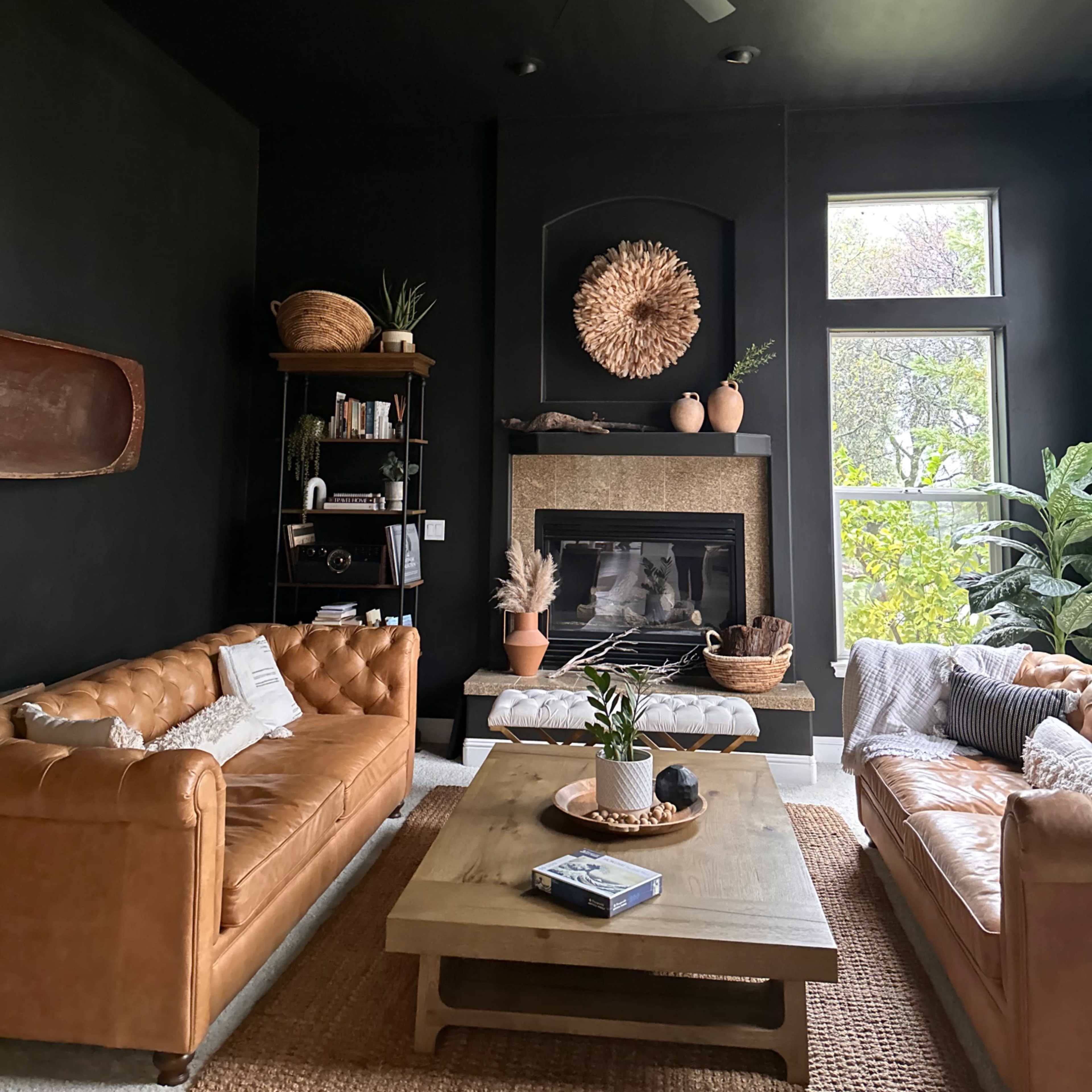 A modern living room with black walls, leather sofas, a wooden coffee table, and a fireplace surrounded by decorative elements.