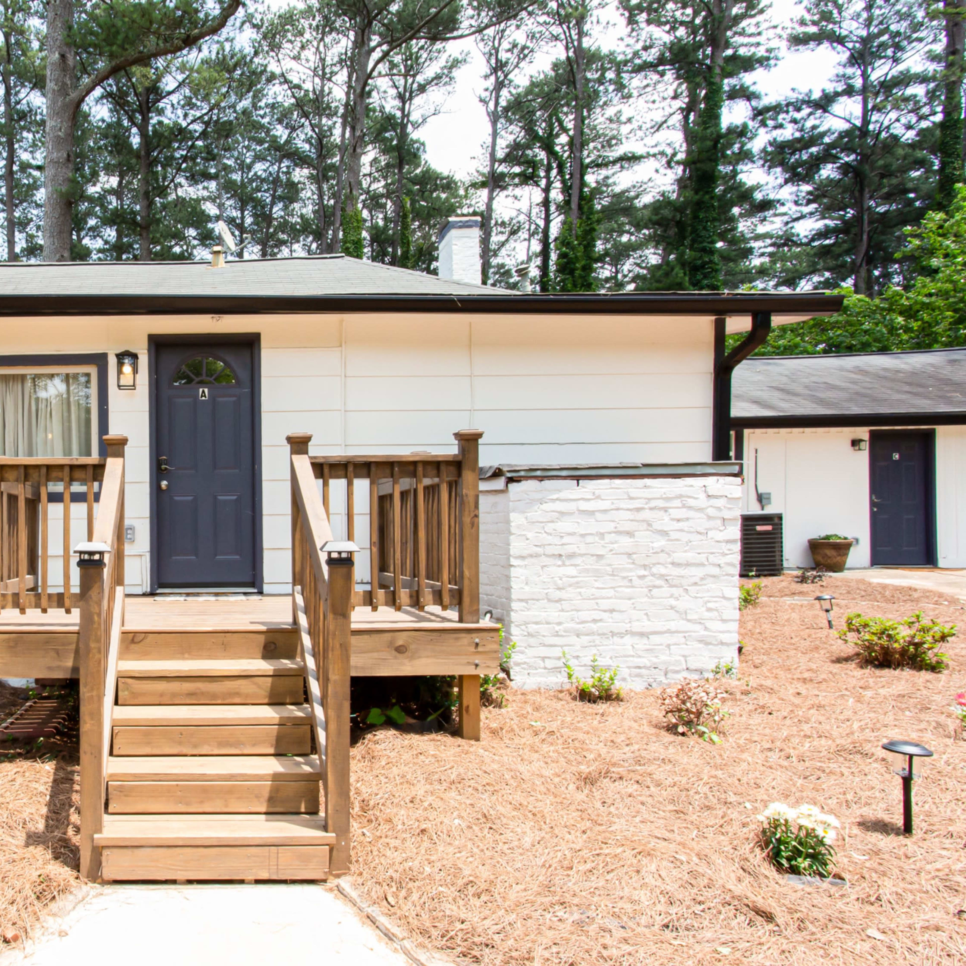 A single-story home with a wooden front porch and steps, surrounded by mulch and small plants.