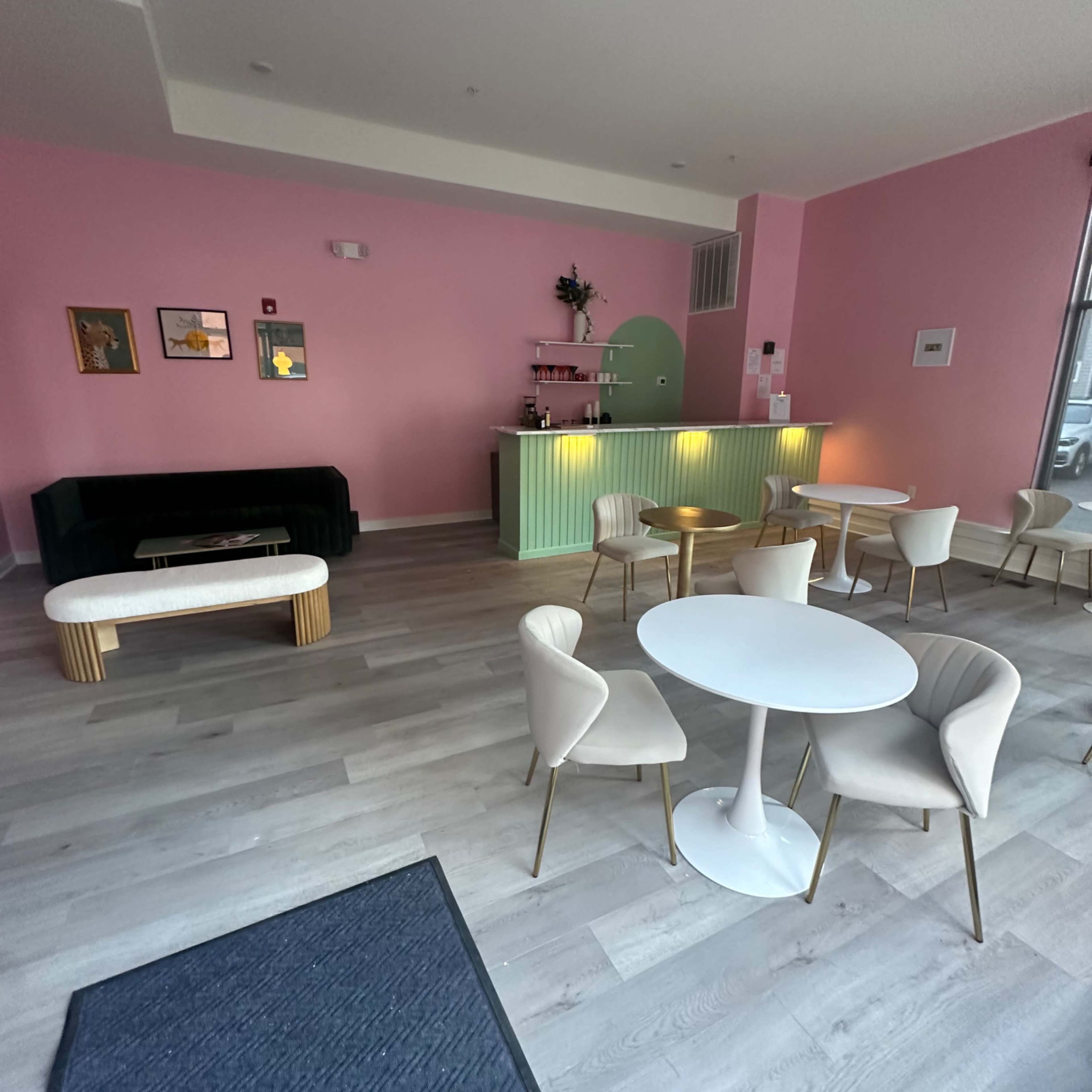 A modern café interior with pink walls, a green counter, and white tables and chairs.