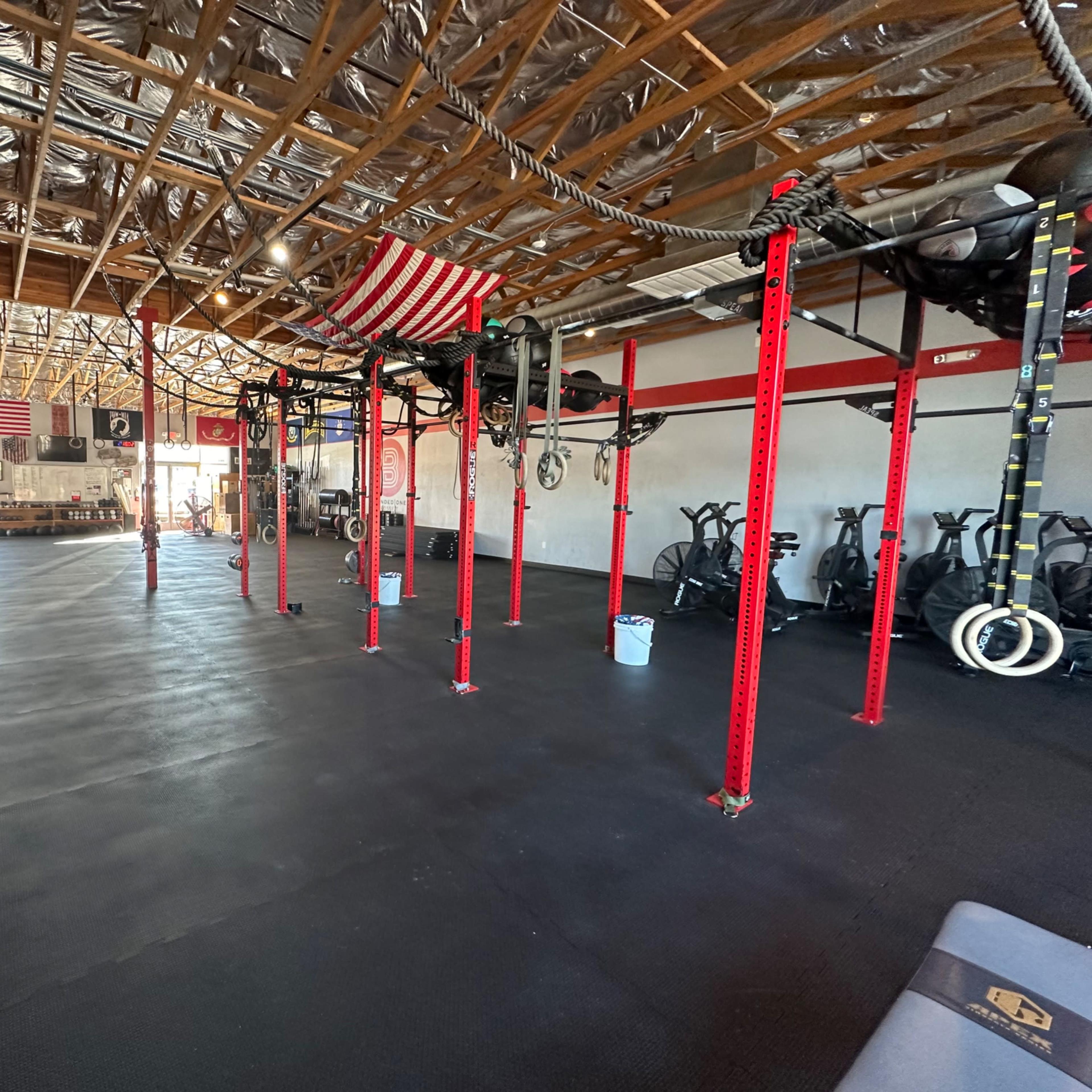 The interior of a gym with red support beams, exercise equipment, and an open floor space.