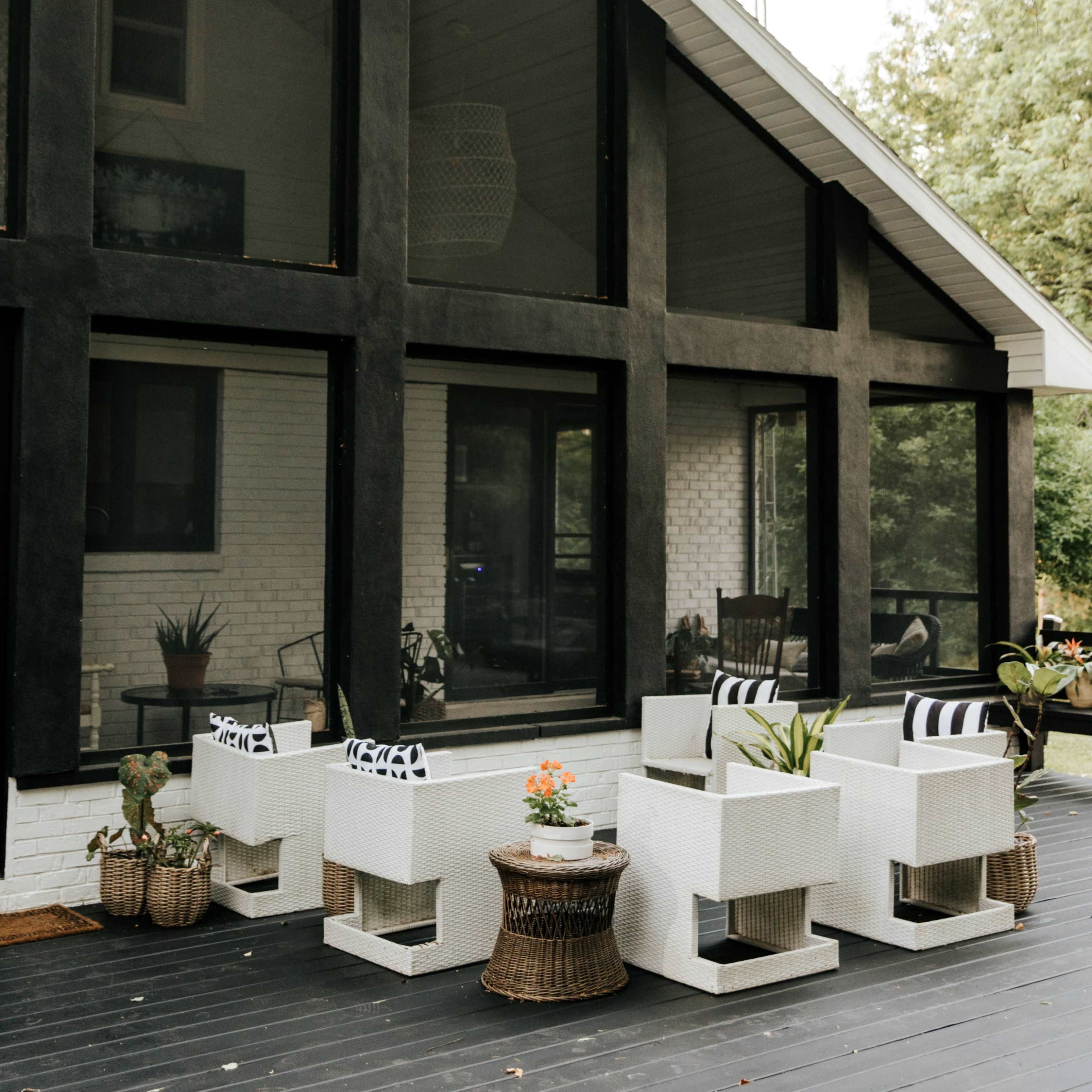A modern outdoor seating area with white chairs and a round table in front of a large glass-walled house.