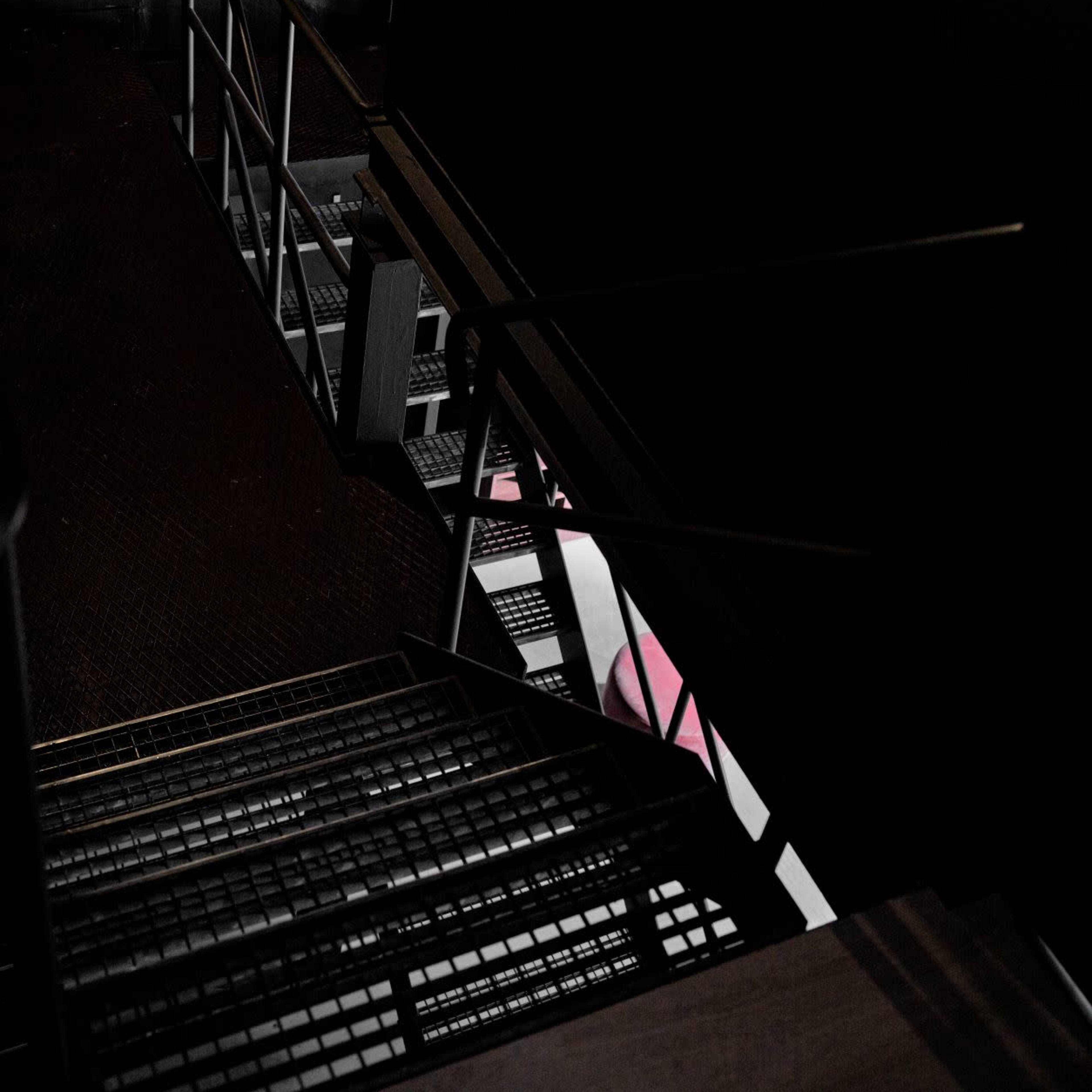 A staircase leads downward in a dark corridor, with metal railings and a textured floor.