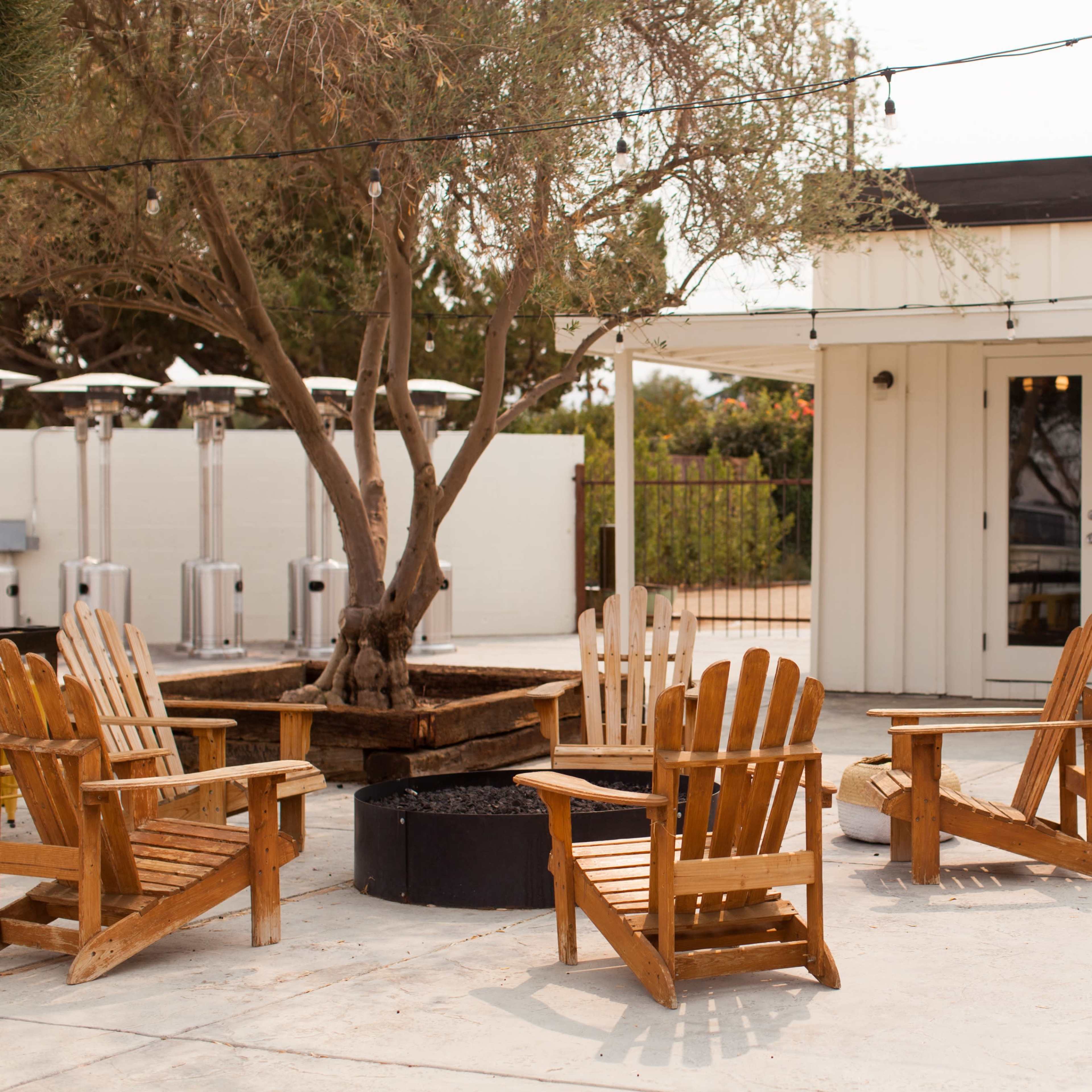 A seating area with wooden Adirondack chairs arranged around a fire pit near a building with glass doors.