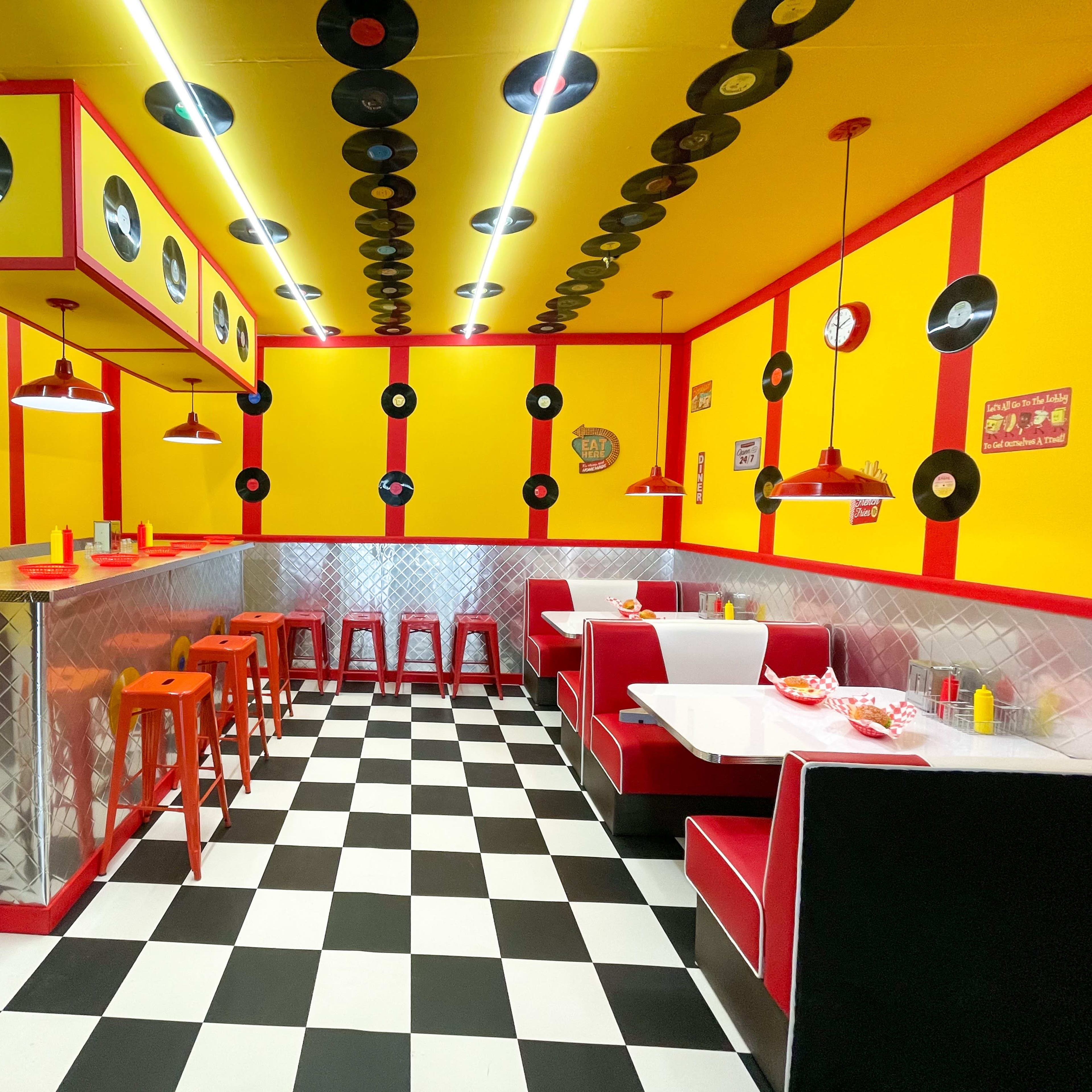 A vintage-style diner features yellow walls adorned with records, red accents, a checkered floor, and both bar and booth seating.