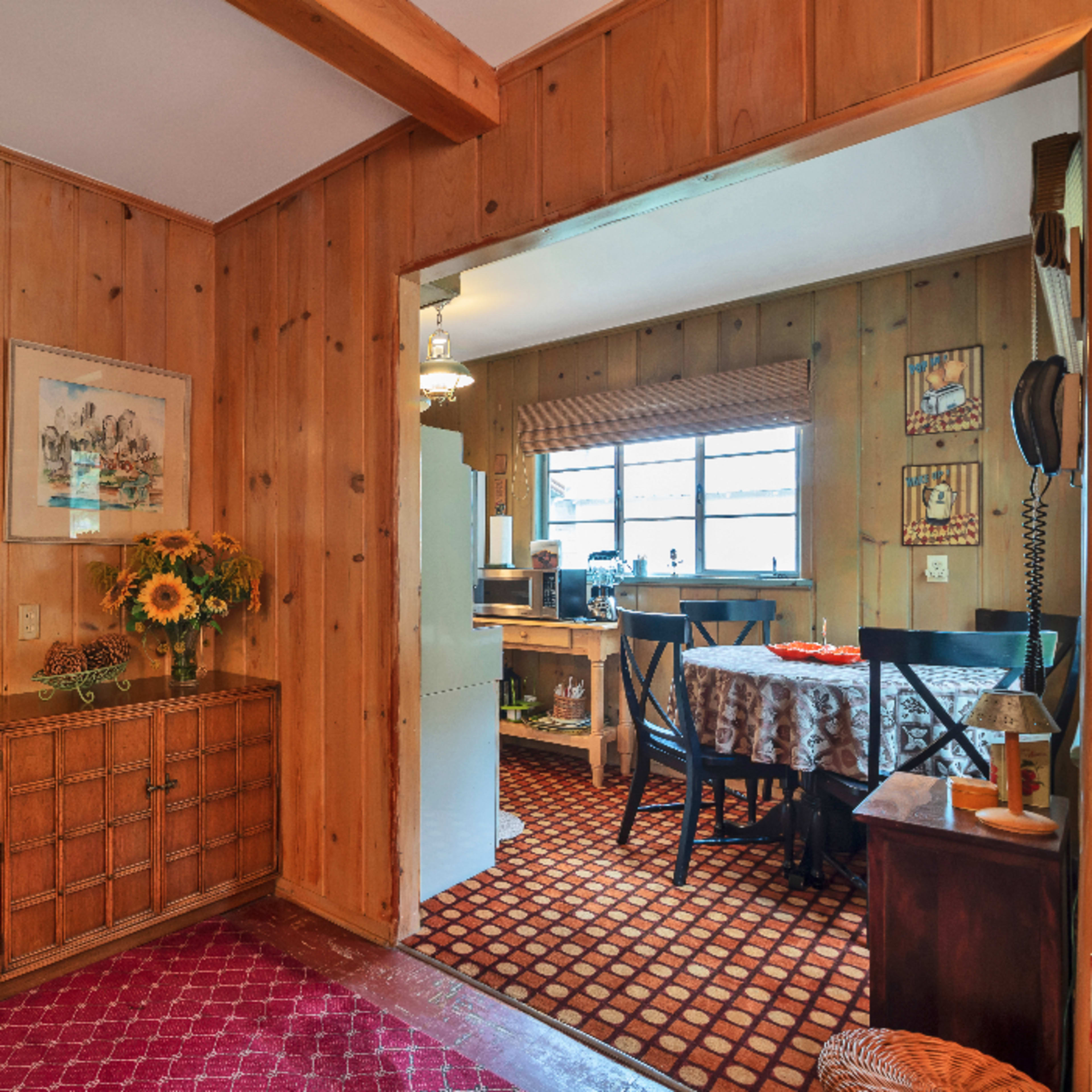 A wooden-paneled interior with a hallway leading to a bathroom on the left and a dining area with a table on the right.