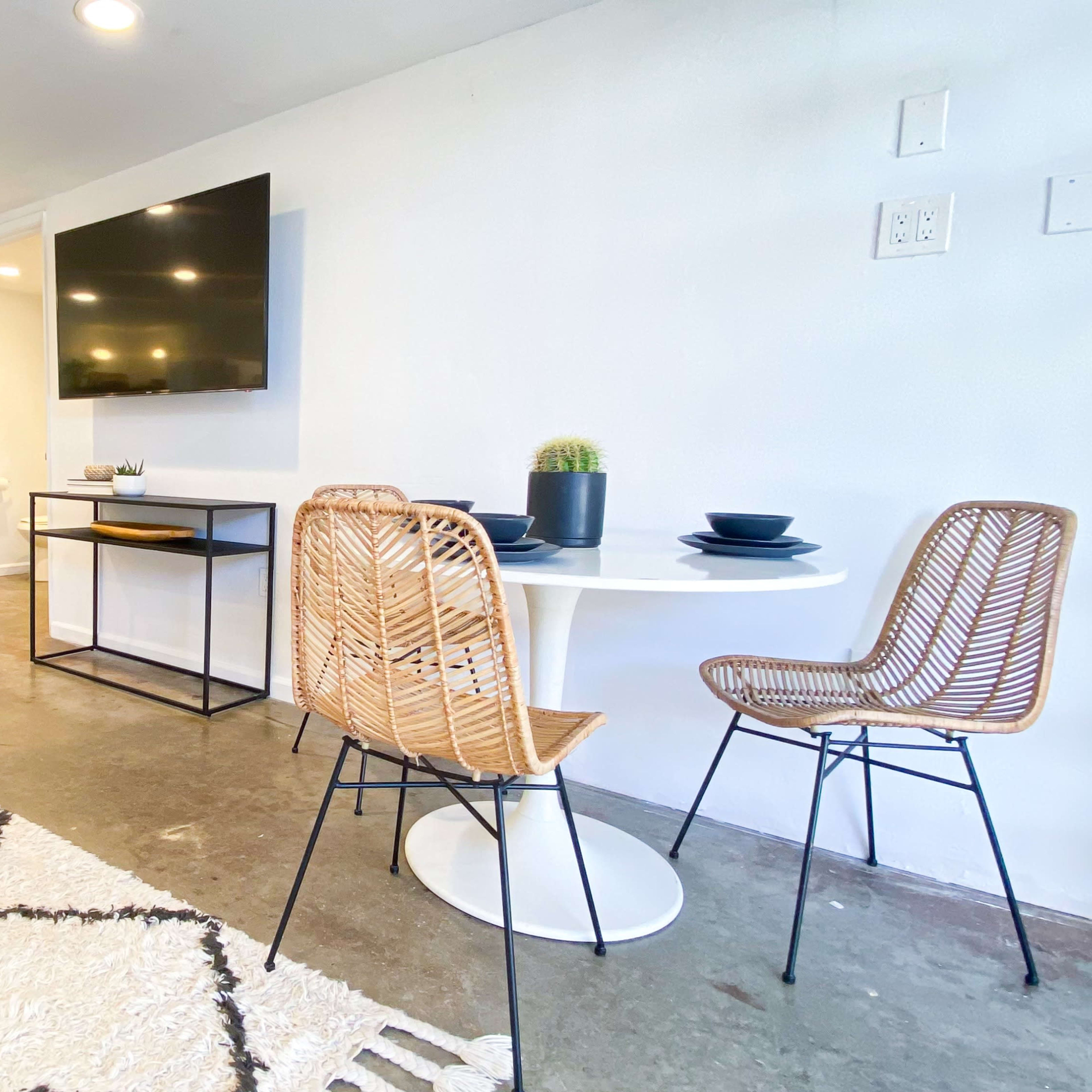 A modern living space features a small dining area with a round table and two chairs, a coffee table, and a wall-mounted television, all set against a backdrop of a minimalist design.