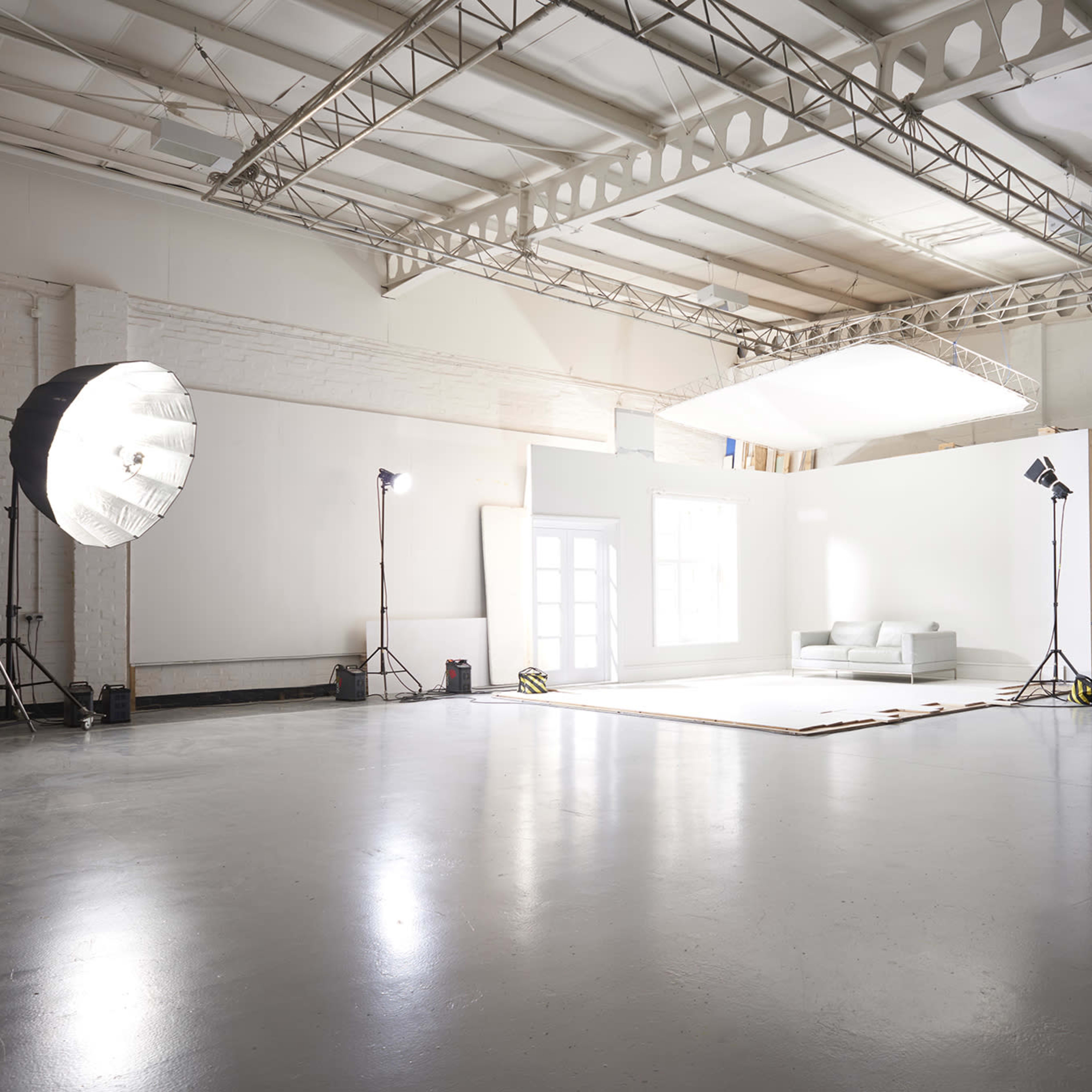 A large photography studio with a white backdrop, lighting equipment, and a simple sofa placed in the center.