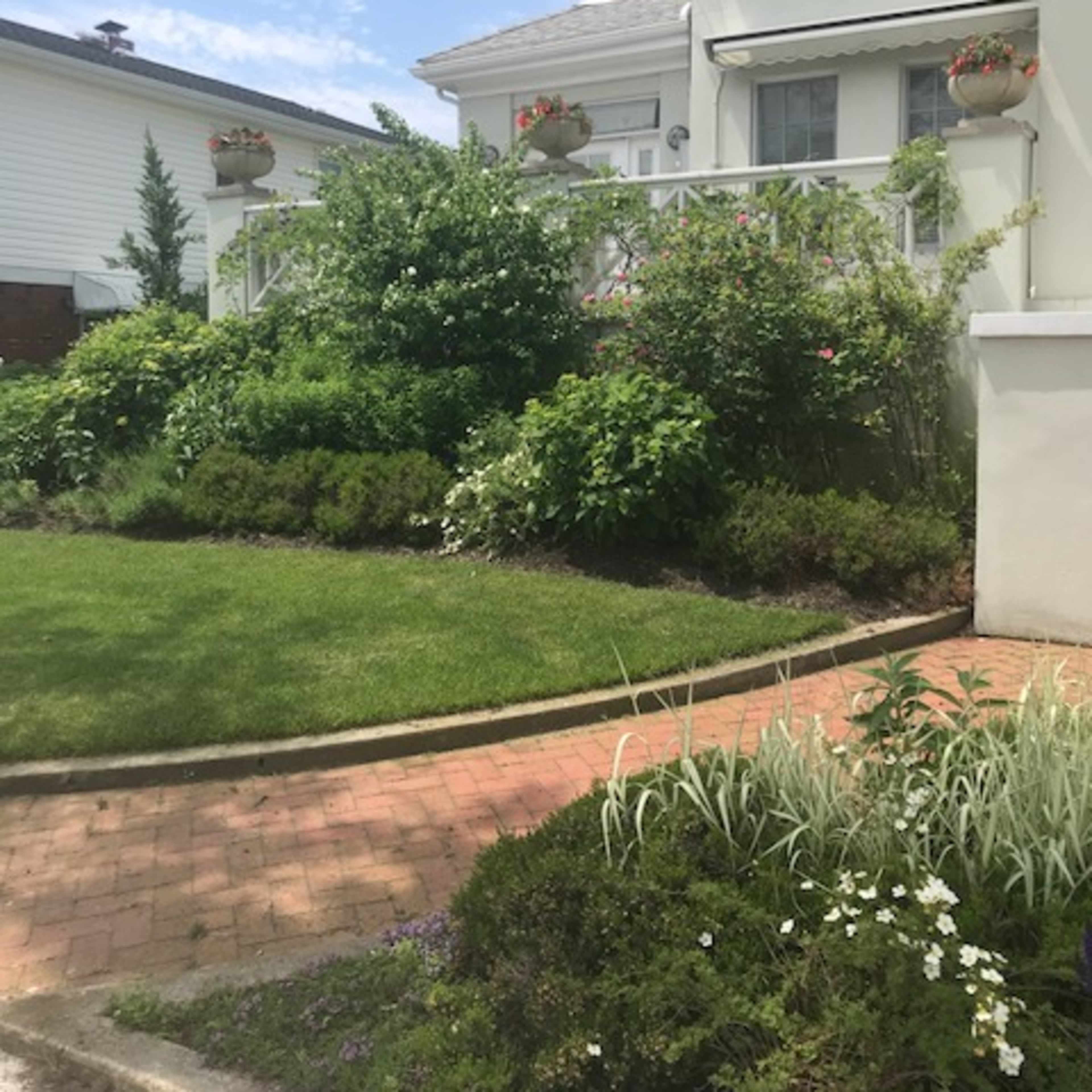 A well-maintained garden with lush greenery and flower pots in front of a white house.
