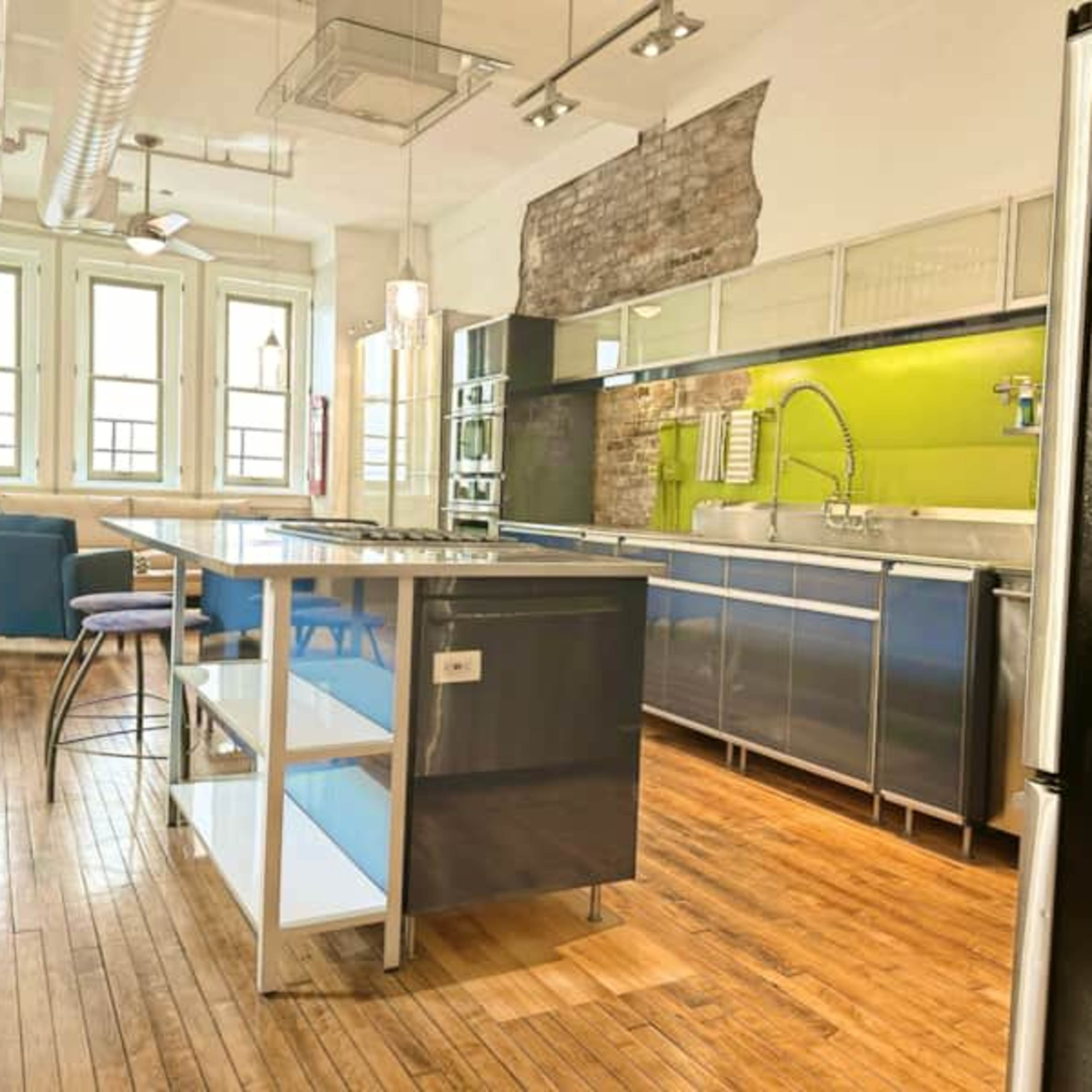 A modern kitchen features stainless steel appliances, a central island, and exposed brick walls with green accents.