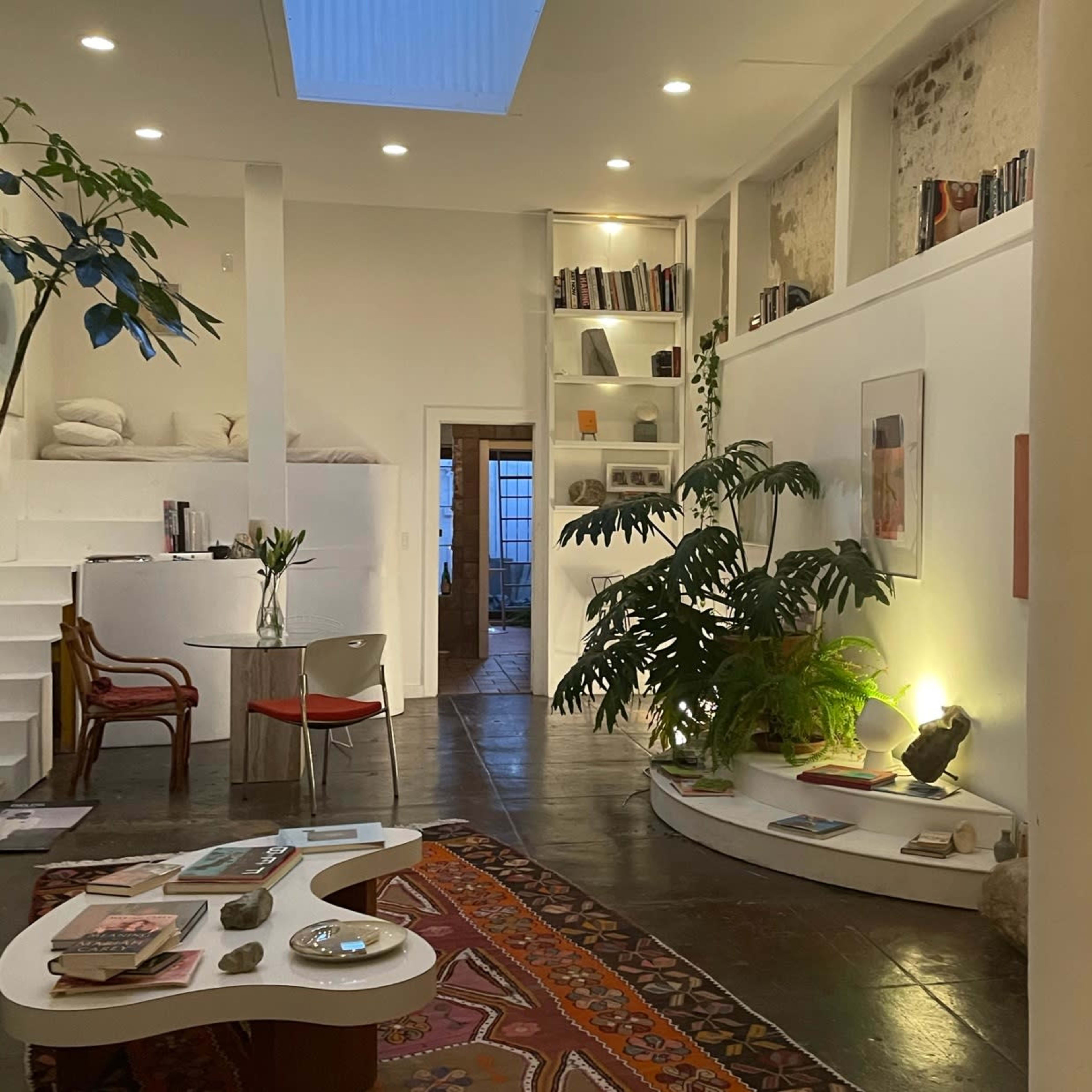 A modern, open living space with a combination of a reading area, plants, and bookshelves against a white backdrop.